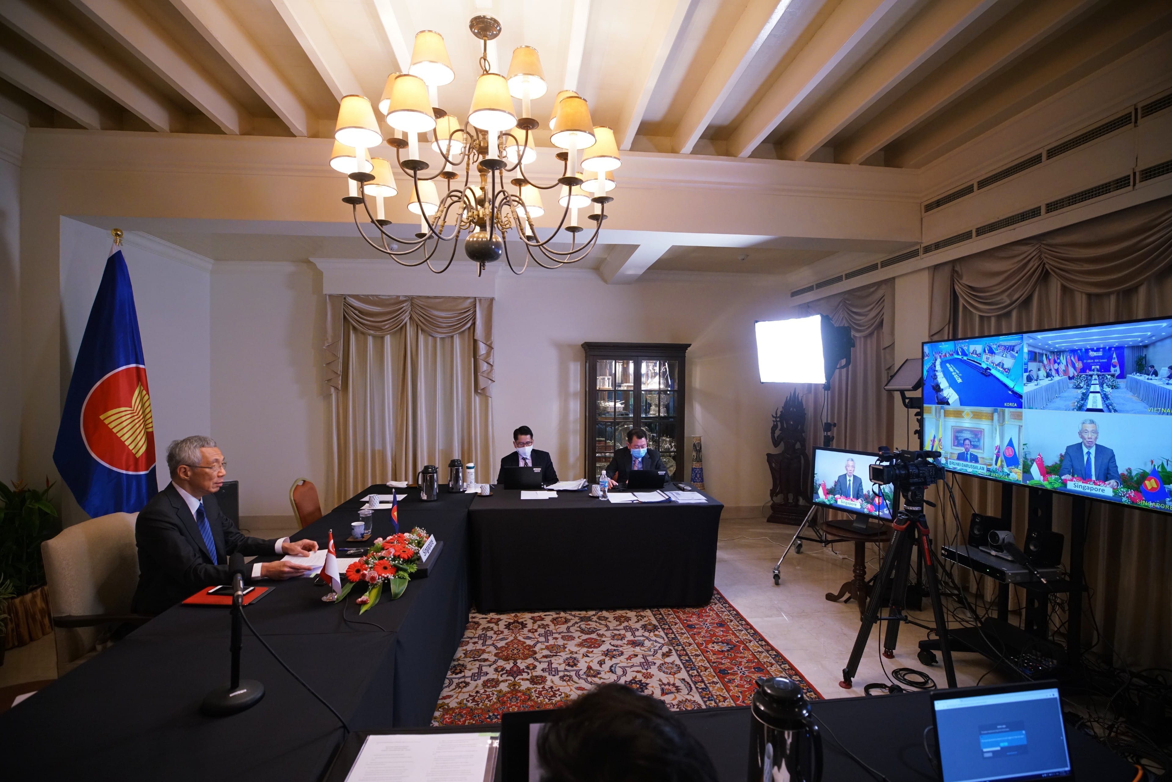 Lee Hsien Loong and others virtually meeting. ASEAN flag visible, screens display video conference.