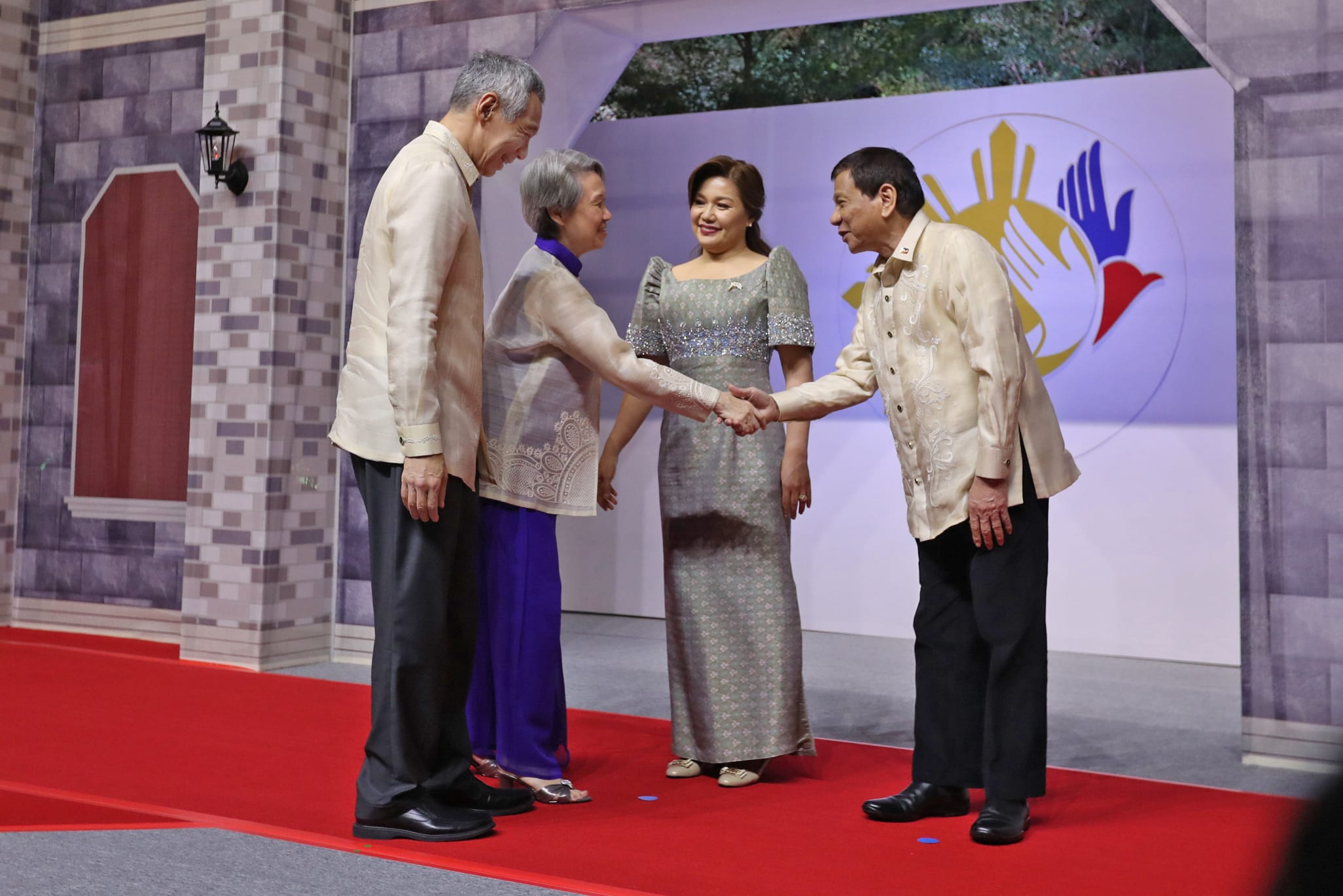 Lee Hsien Loong and Duterte shake hands on a red carpet in front of a hand-themed logo.