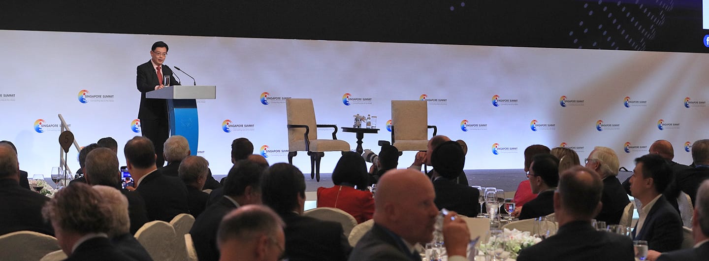 Man at podium speaks to seated audience at Singapore Summit event.