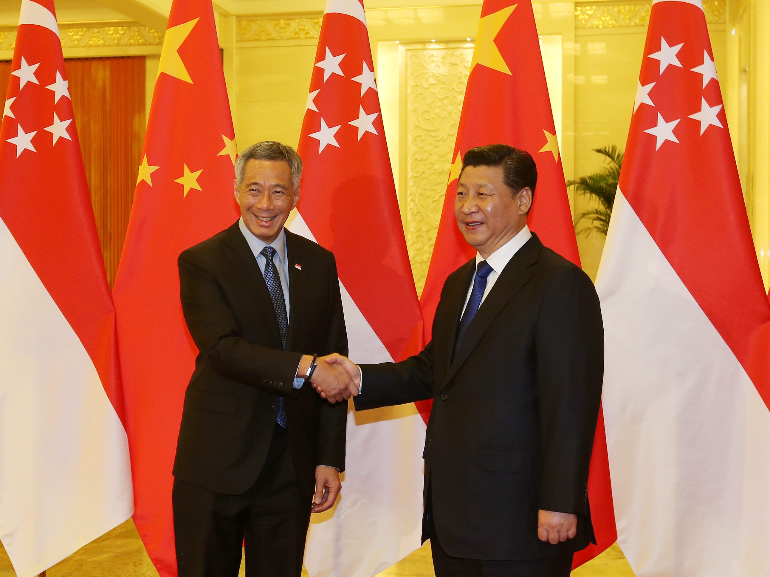 Lee Hsien Loong and Xi Jinping shake hands before Singapore and China flags.