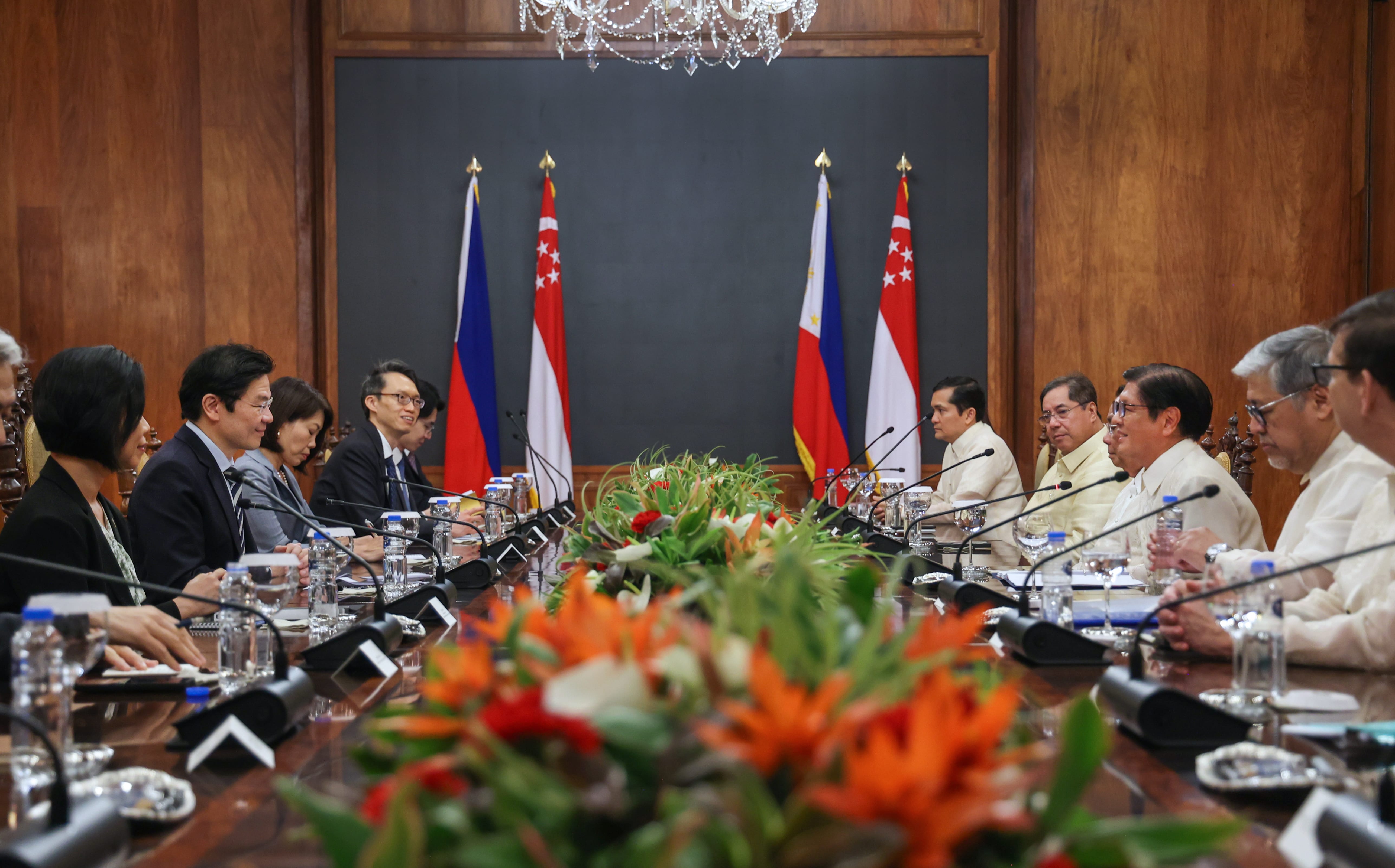 People sit at a long table, with flags of the Philippines and Singapore behind them.