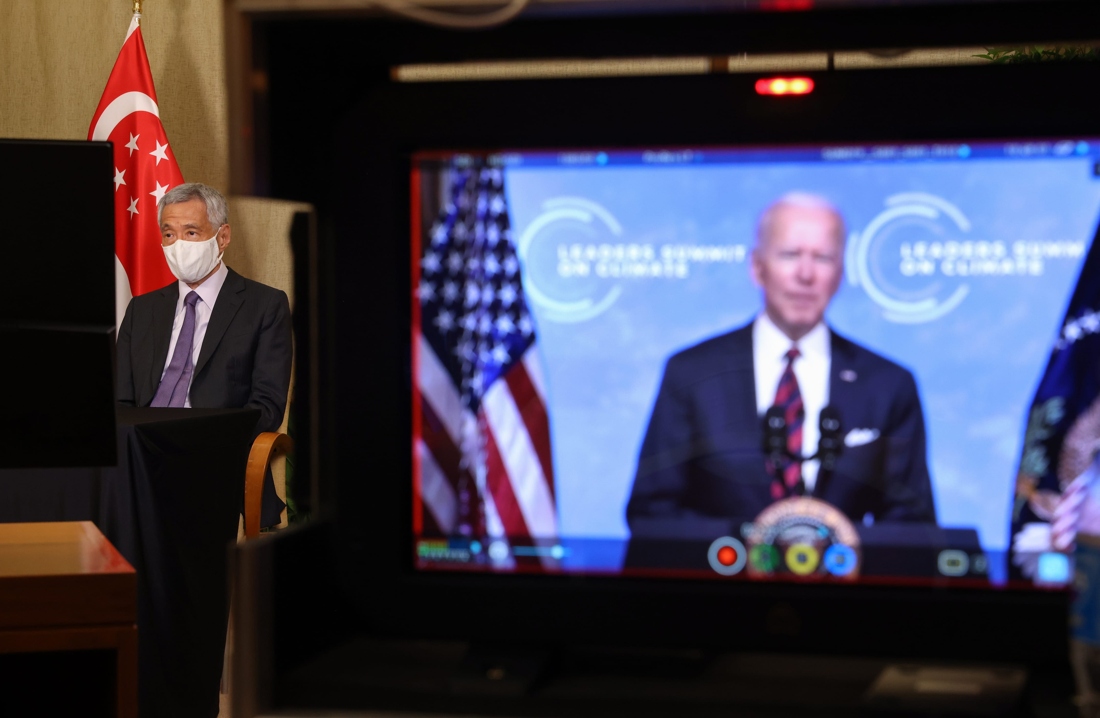 Lee Hsien Loong with mask, Singapore flag; TV displays Joe Biden "Leaders Summit on Climate".
