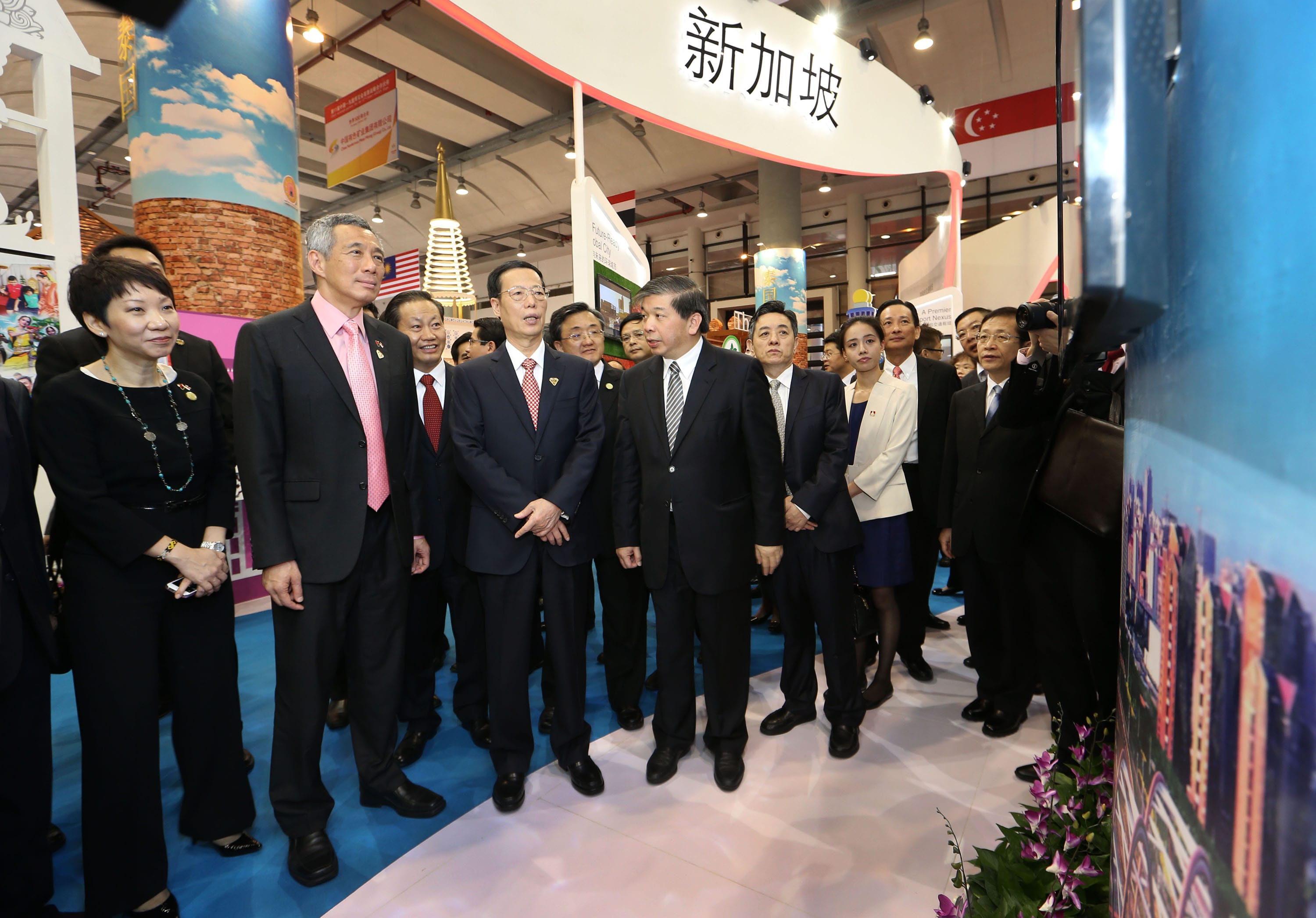 Group of people in suits at Singapore booth with Chinese text at an indoor event.