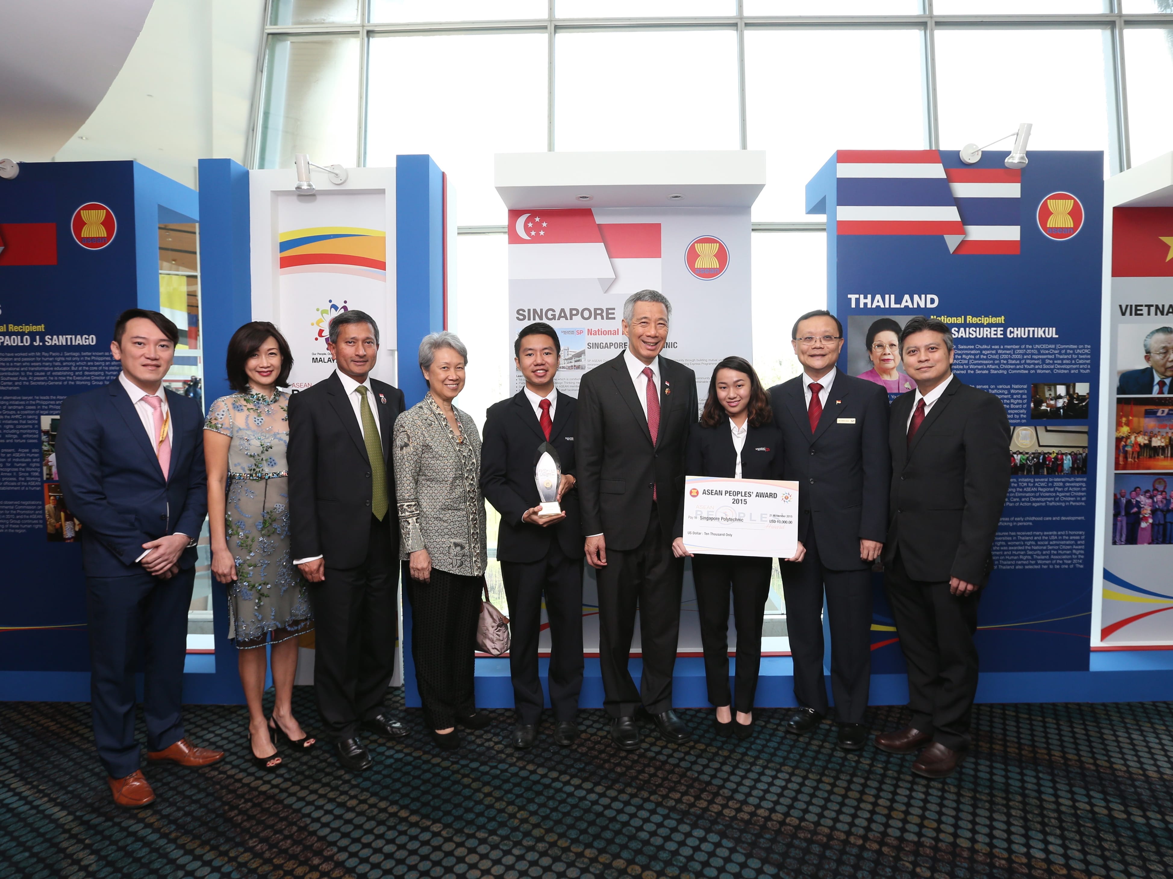 Group poses with Singapore's Prime Minister Lee Hsien Loong, holding awards, in front of country displays.