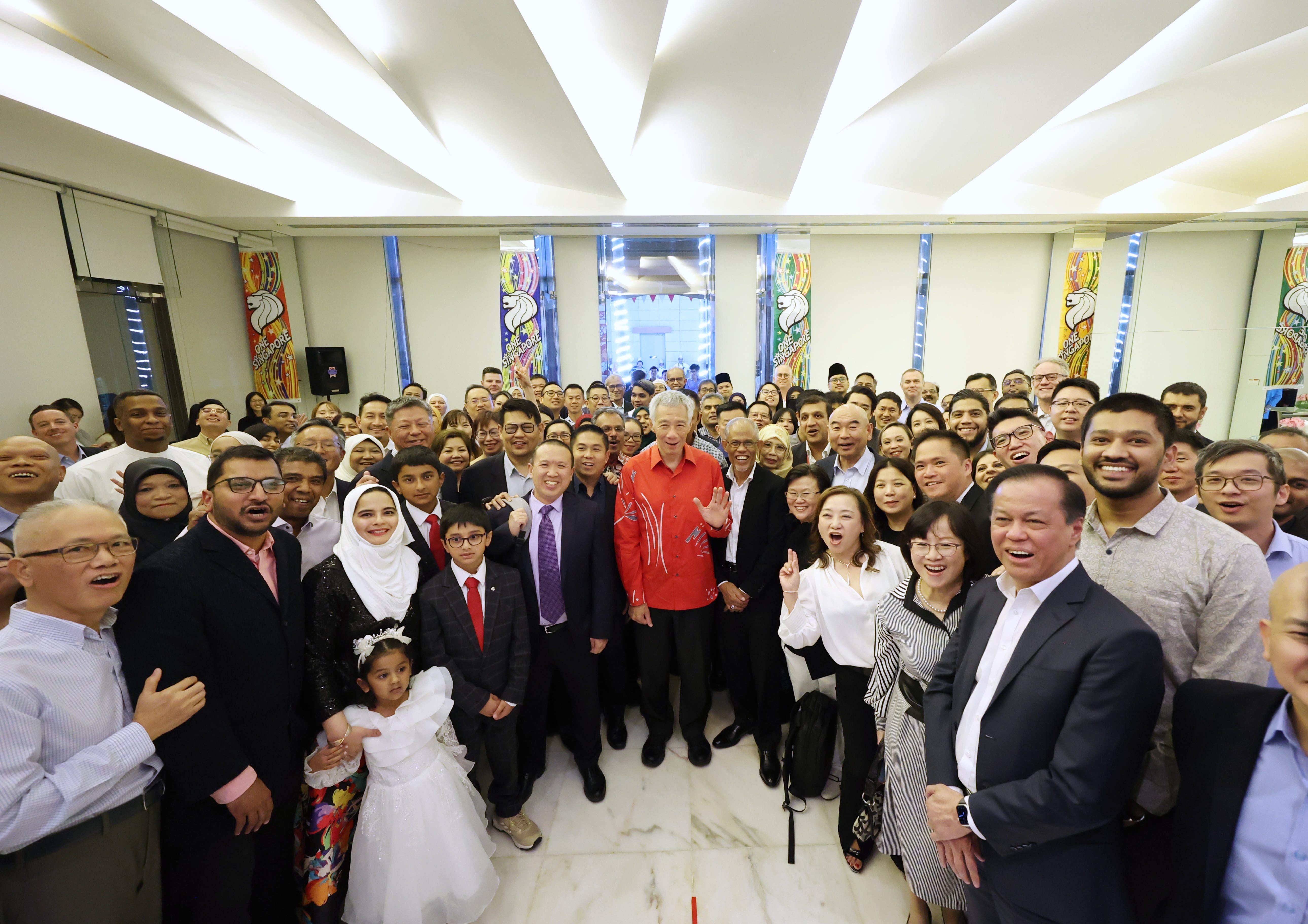 Lee Hsien Loong with a crowd of people posing for a group photo in a bright room.