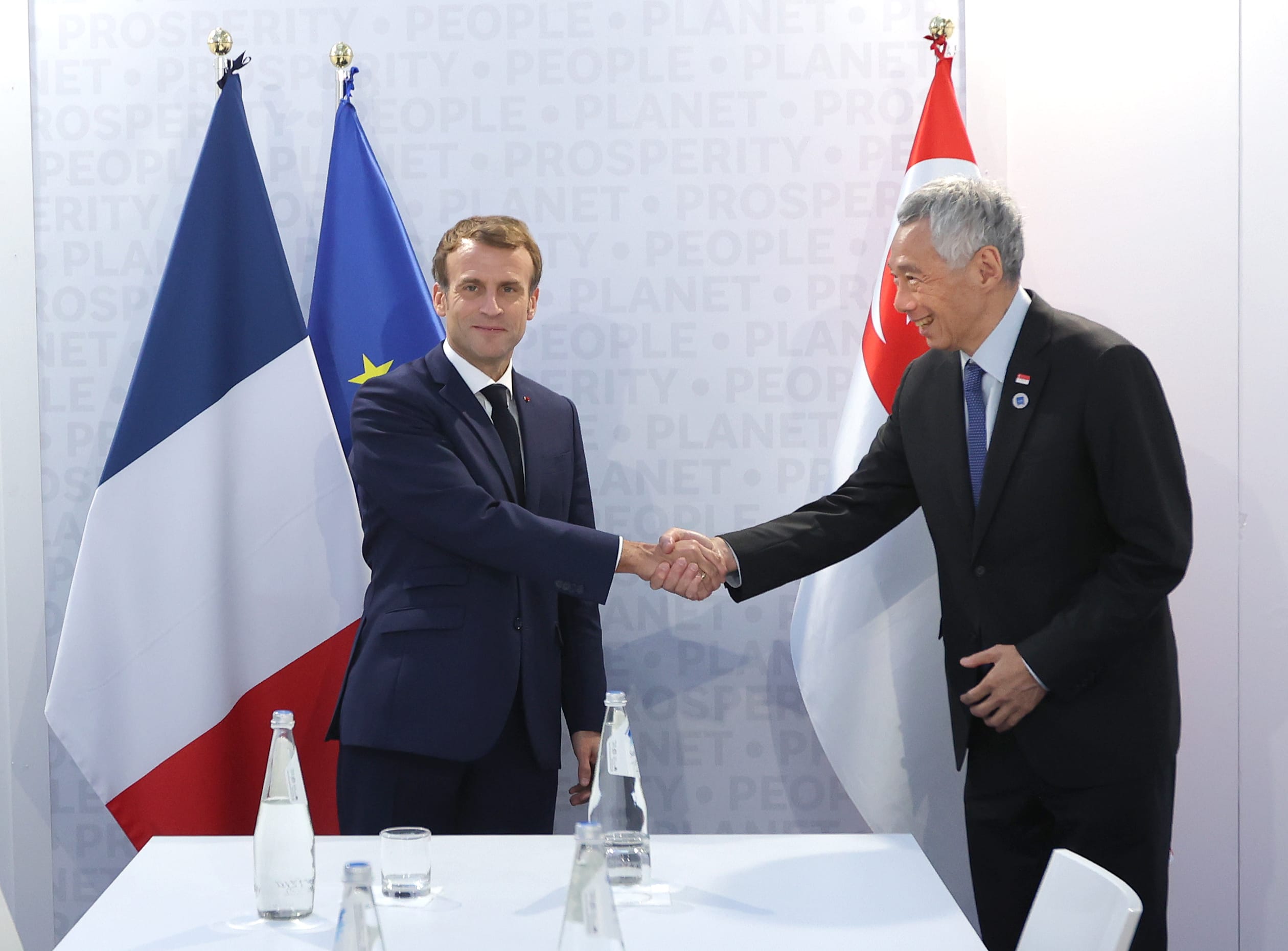 Emmanuel Macron and Lee Hsien Loong shaking hands. Flags of France, EU, and Singapore behind them.