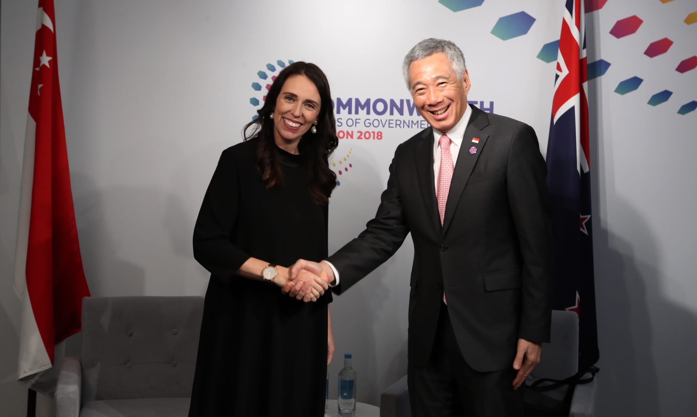 Jacinda Ardern and Lee Hsien Loong shake hands. Singapore and New Zealand flags behind.
