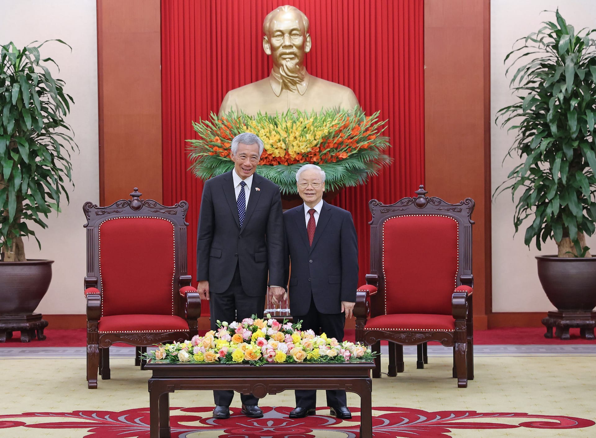 Lee Hsien Loong and Nguyen Phu Trong in suits, holding hands before a Ho Chi Minh bust.