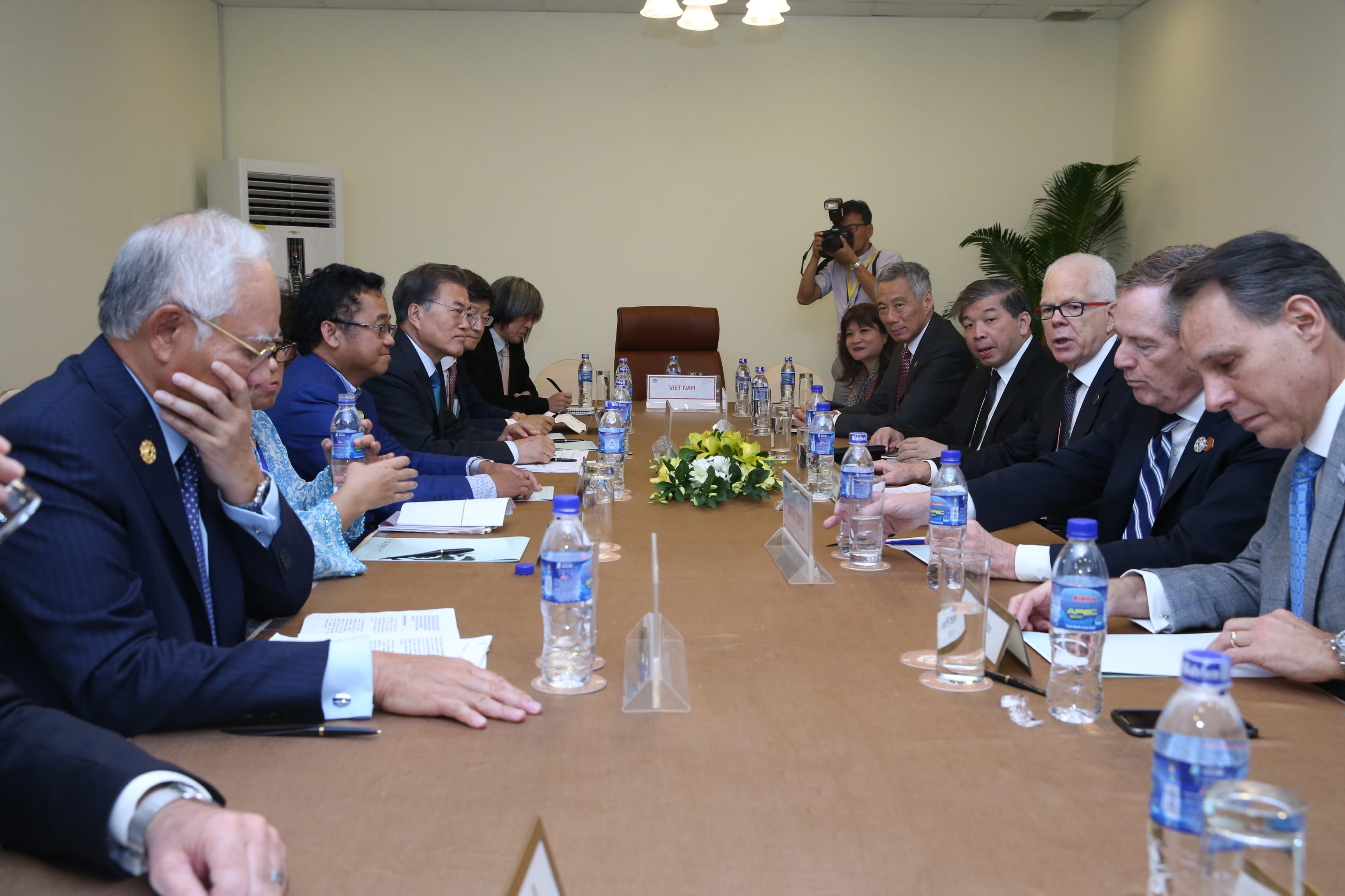 People at a conference table with "Viet Nam" placard, water bottles, and a photographer.