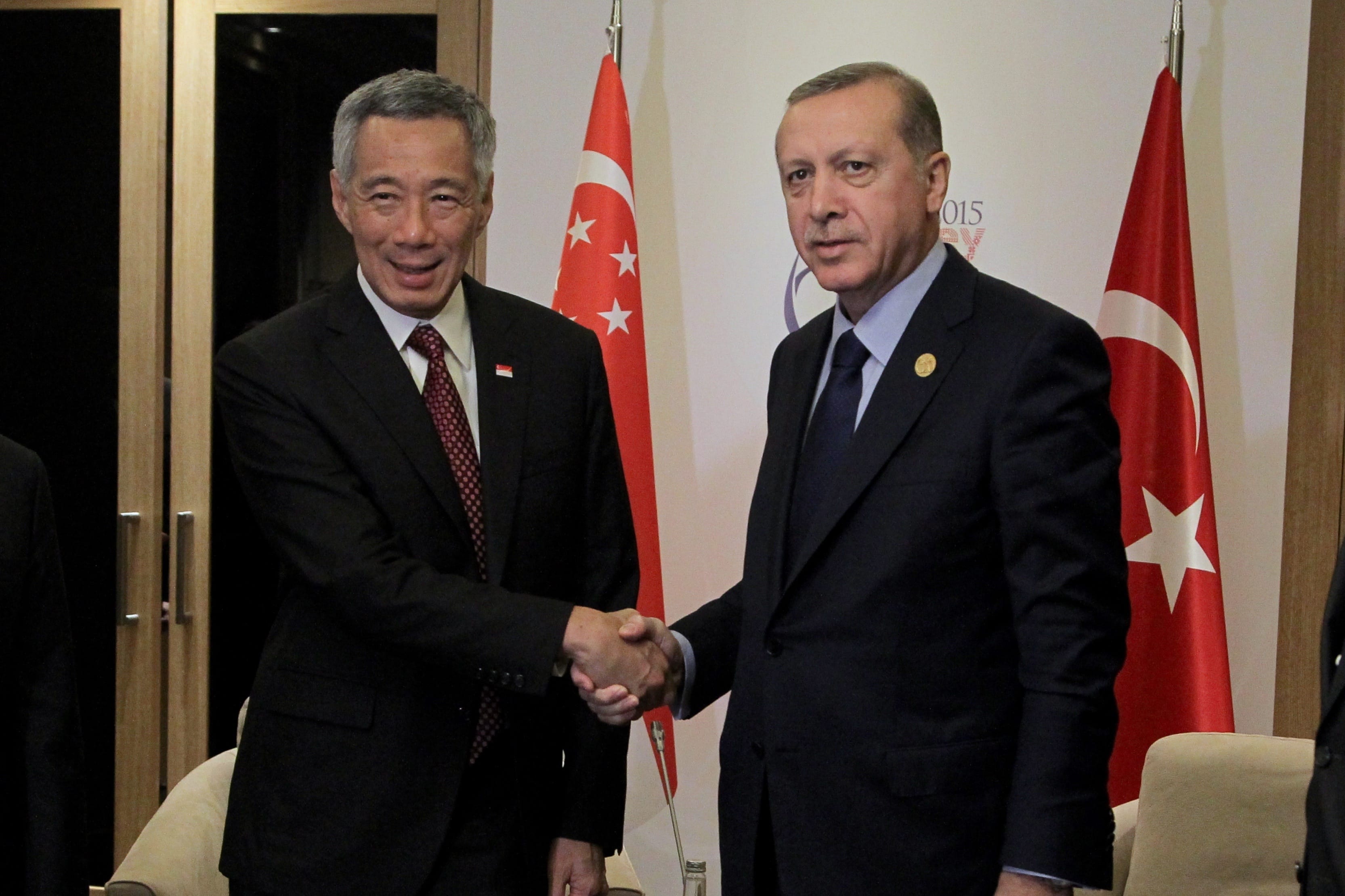Lee Hsien Loong and Recep Tayyip Erdoğan in suits shake hands, standing before Singapore and Turkey flags.