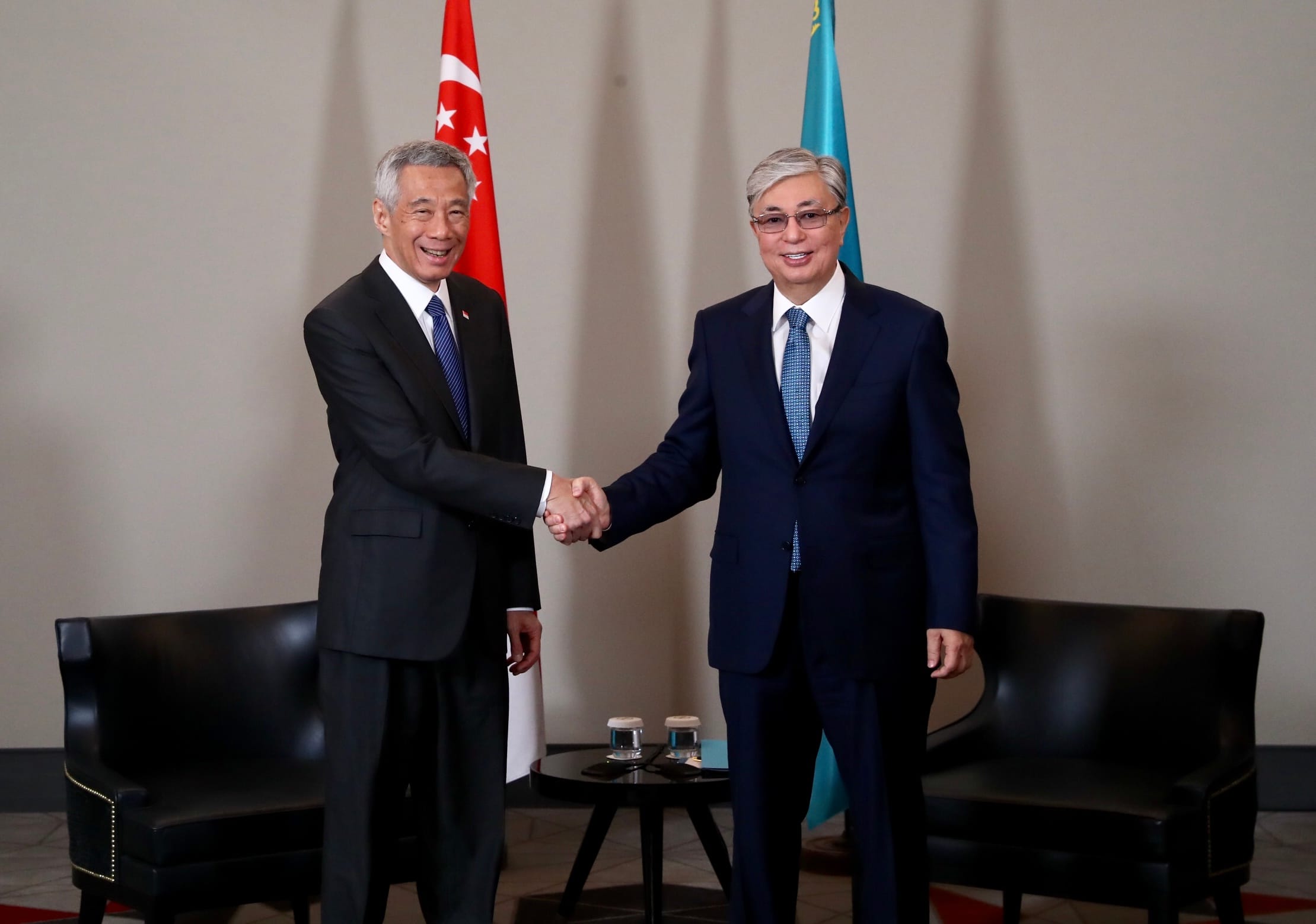 Two men in suits shaking hands with flags of Singapore and Kazakhstan behind.