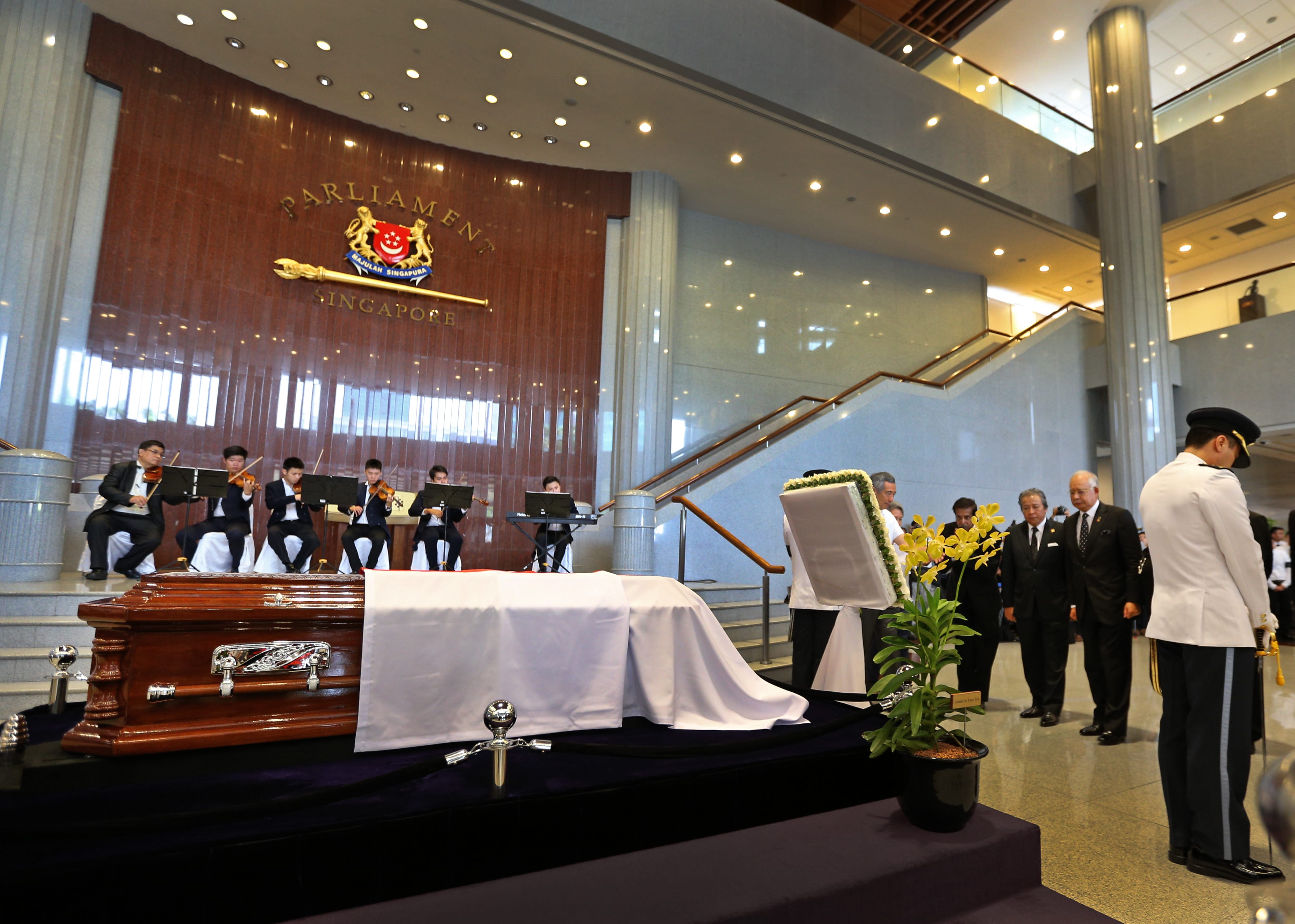 Casket on a platform in Parliament of Singapore with musicians and officials present.