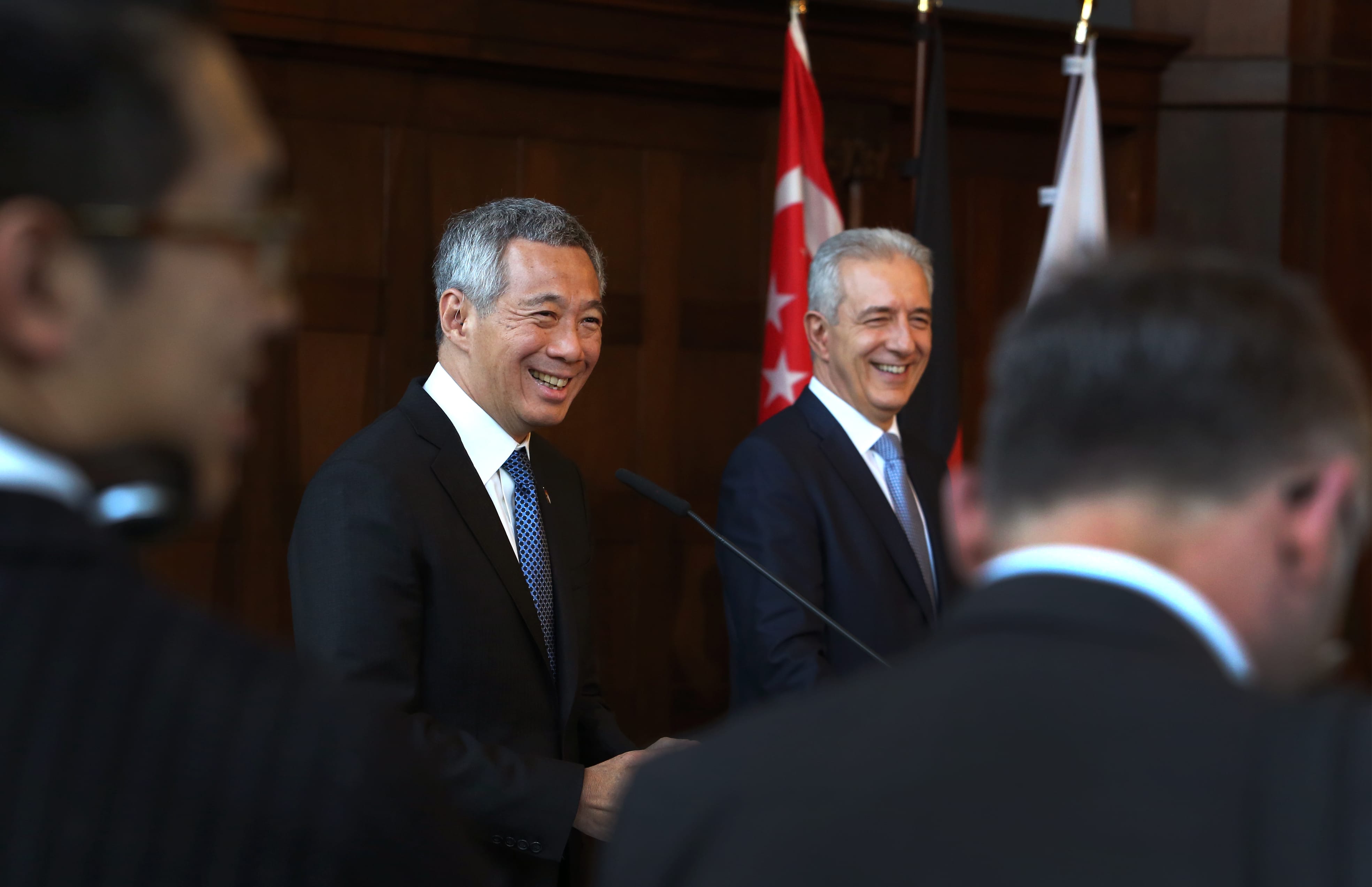 Lee Hsien Loong and another man in suits smile before flags.