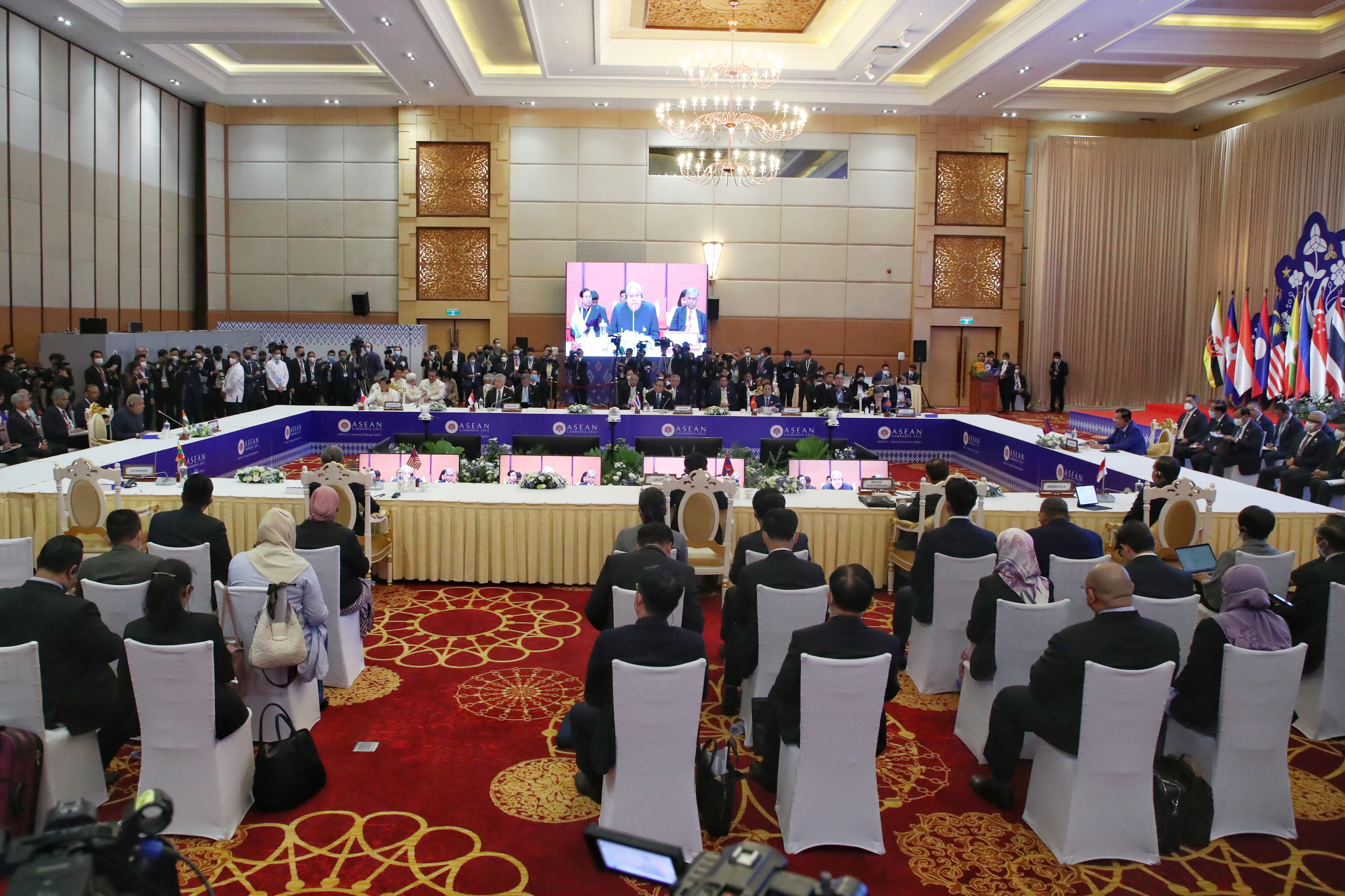 Large conference room with seated attendees facing tables labeled "ASEAN" and country names, flags in background.