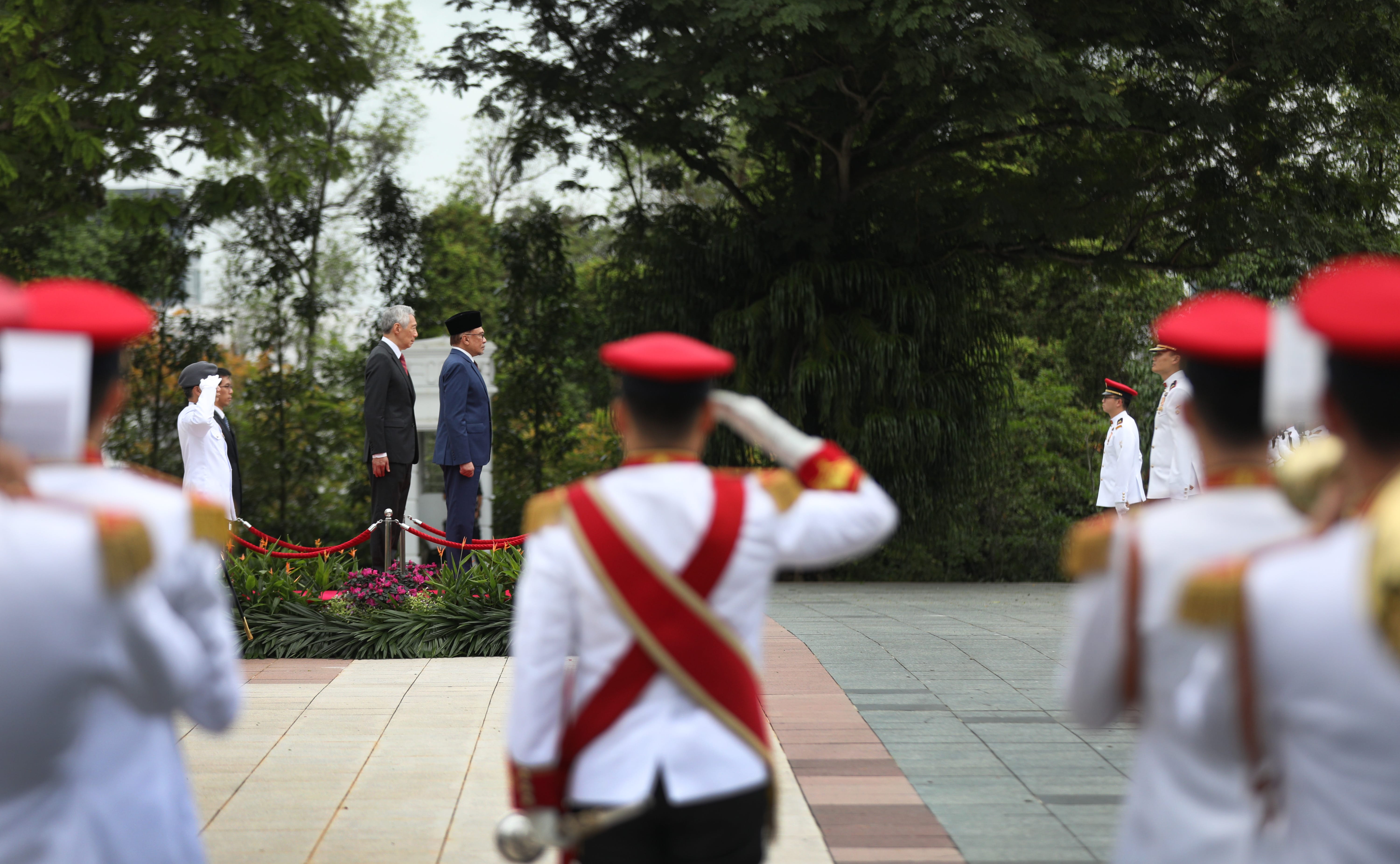 Guards in white uniforms and red hats salute Lee Hsien Loong and Anwar Ibrahim.