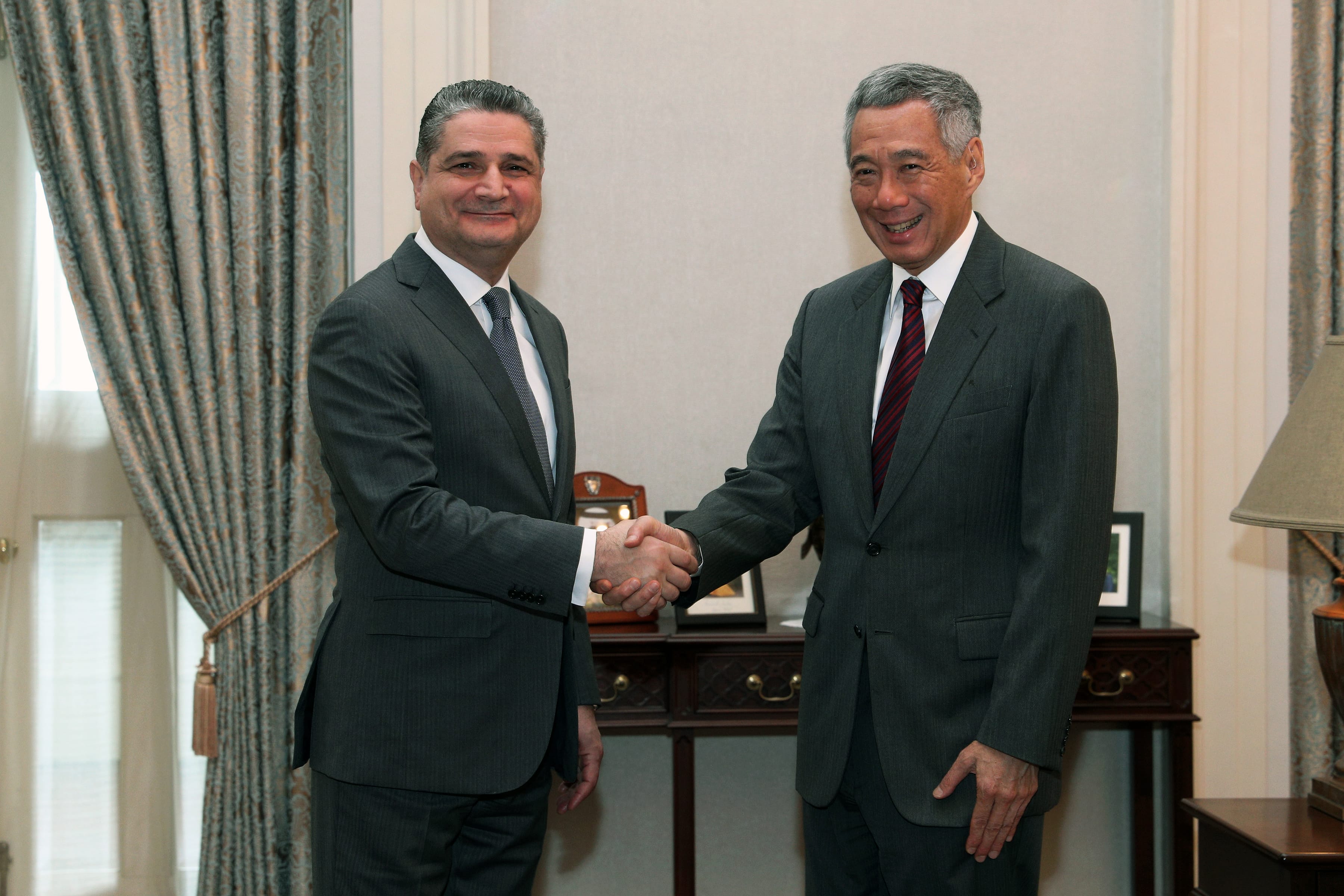 Two men in suits shaking hands in a formal setting.