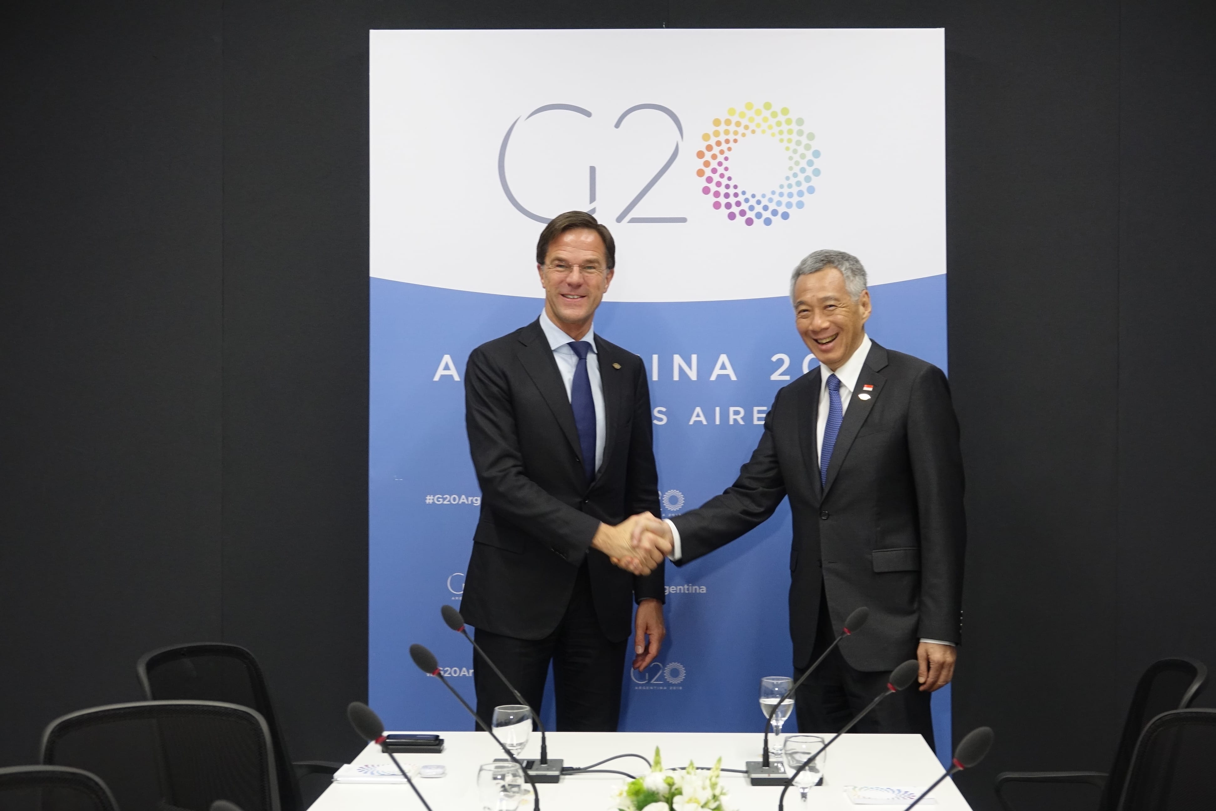 Mark Rutte and Lee Hsien Loong shake hands in front of a G20 Argentina backdrop.