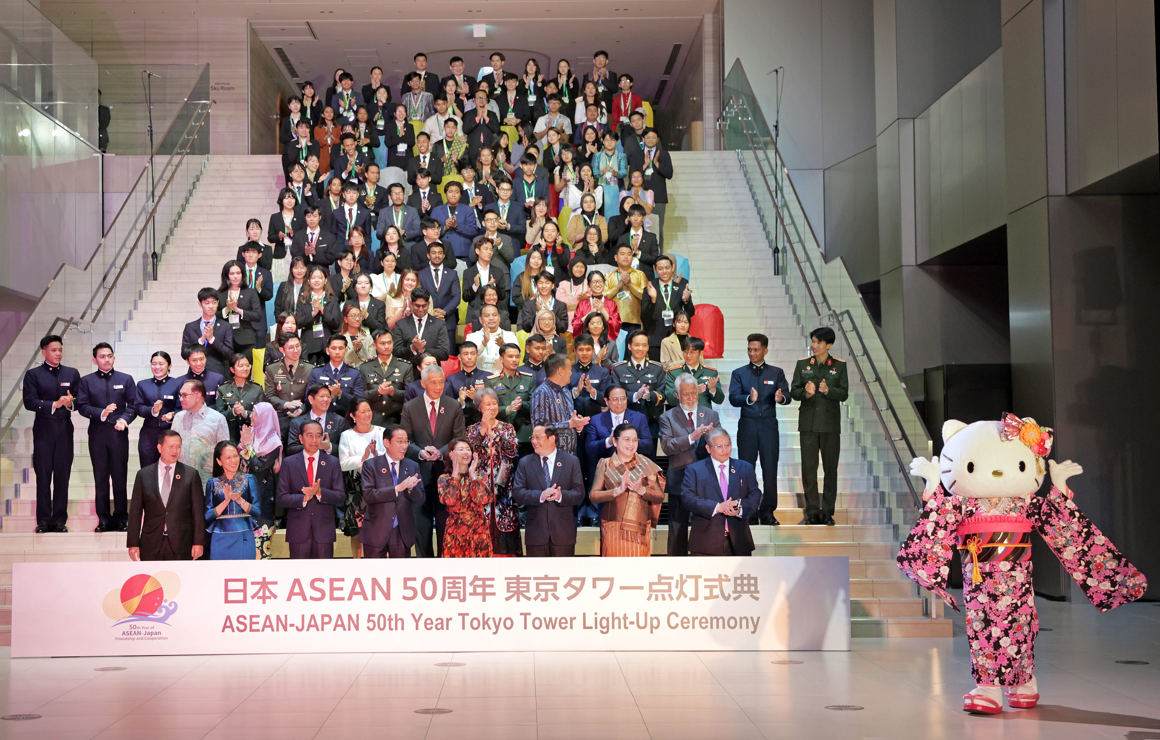Large group of people on stairs behind Hello Kitty in kimono; "ASEAN-Japan 50th Year" sign.