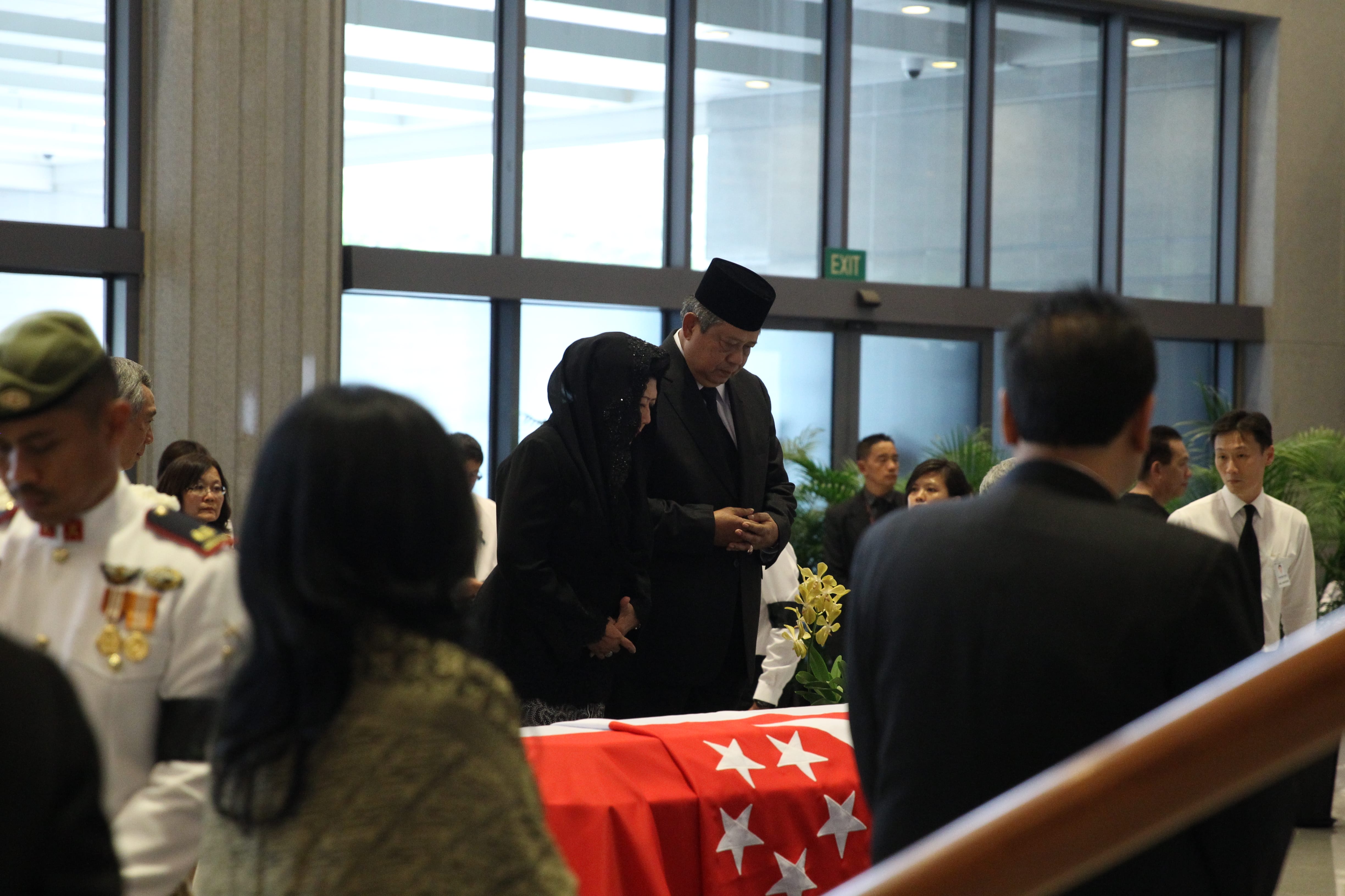 Attendees in dark clothing near coffin draped with Singapore flag.