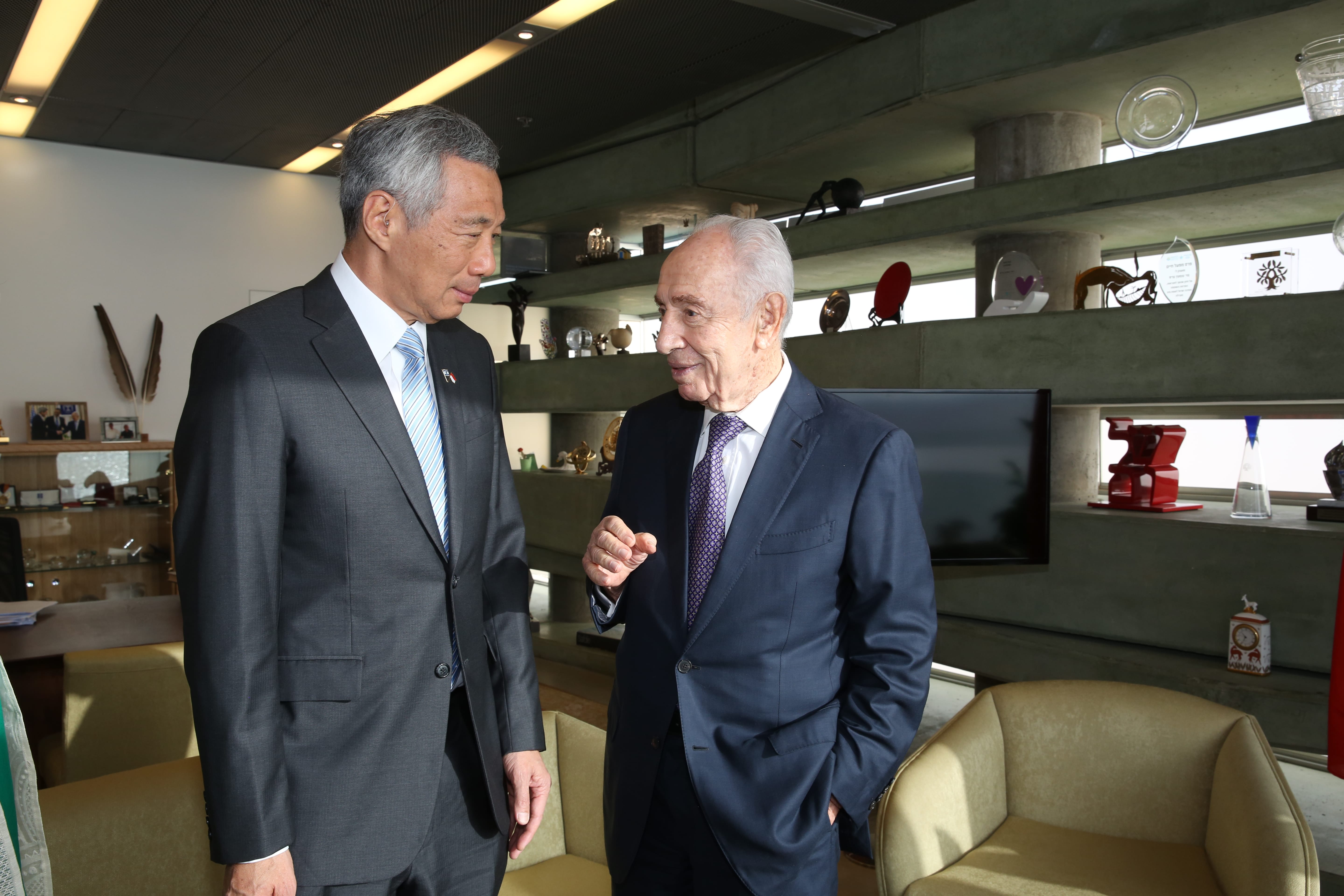 Lee Hsien Loong and Shimon Peres in suits, standing indoors and talking.