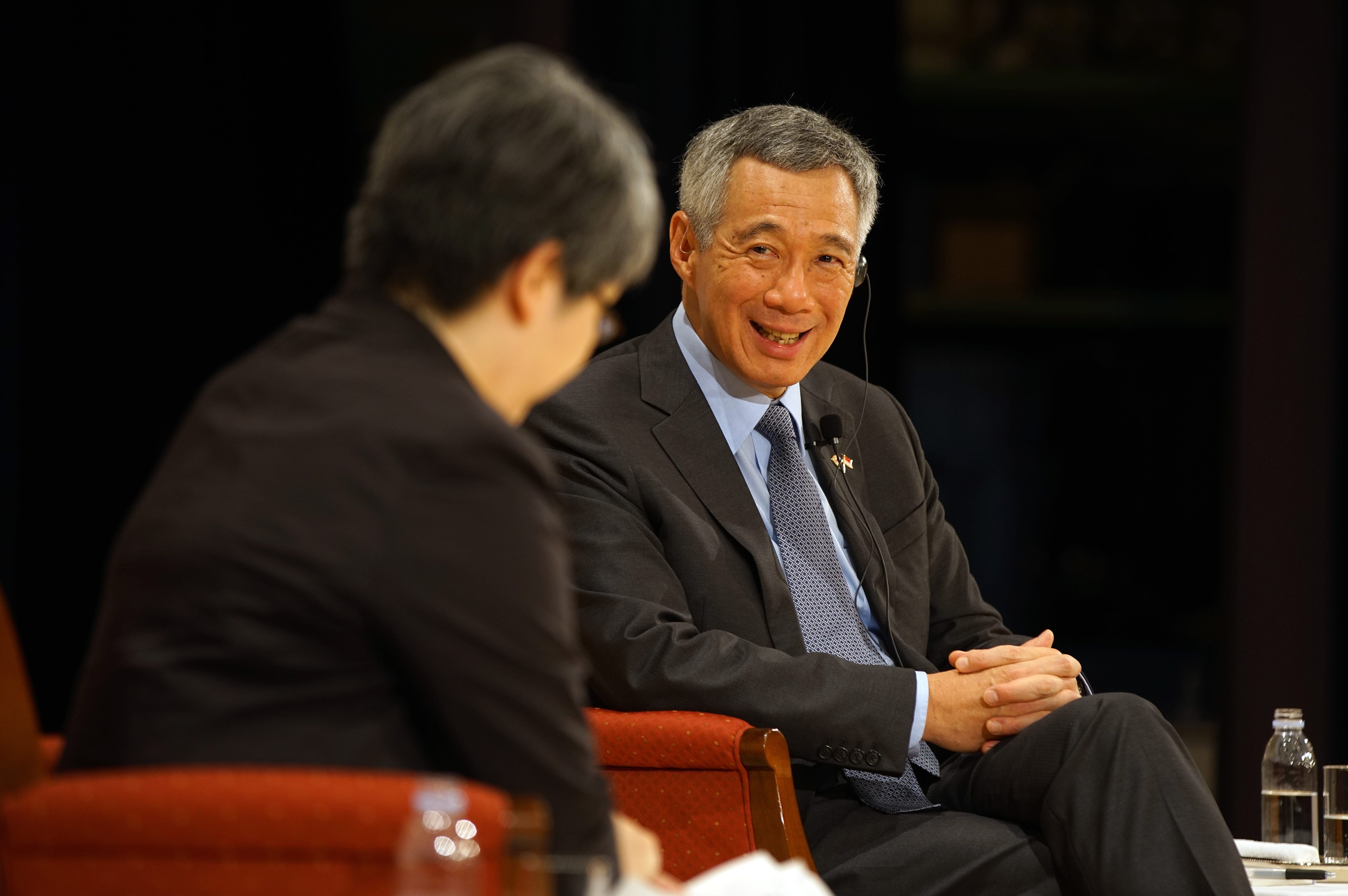 Lee Hsien Loong in suit, seated on red chair, looking at person in dark suit.