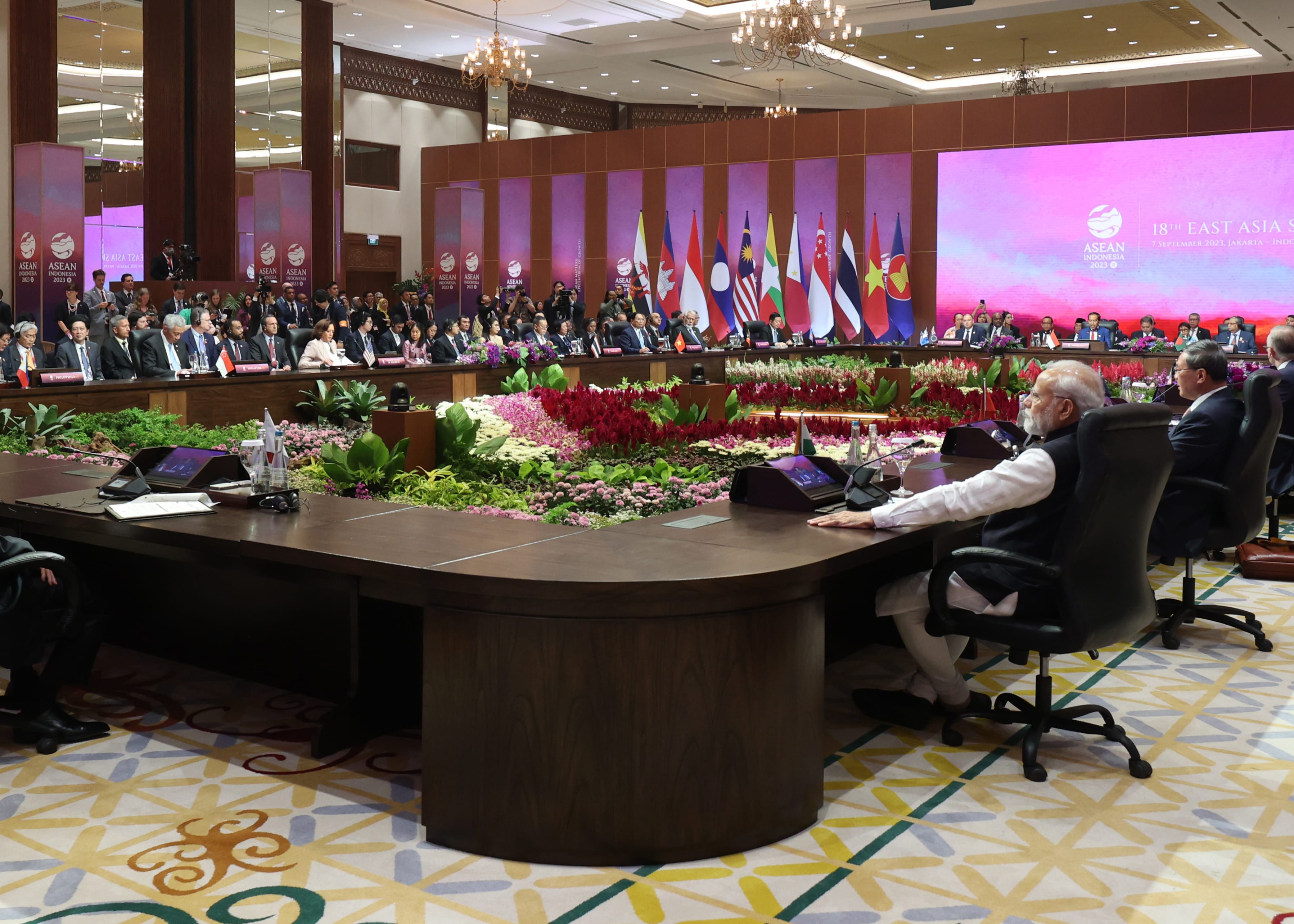 Meeting room with world leaders at long table; country flags and ASEAN logo visible.