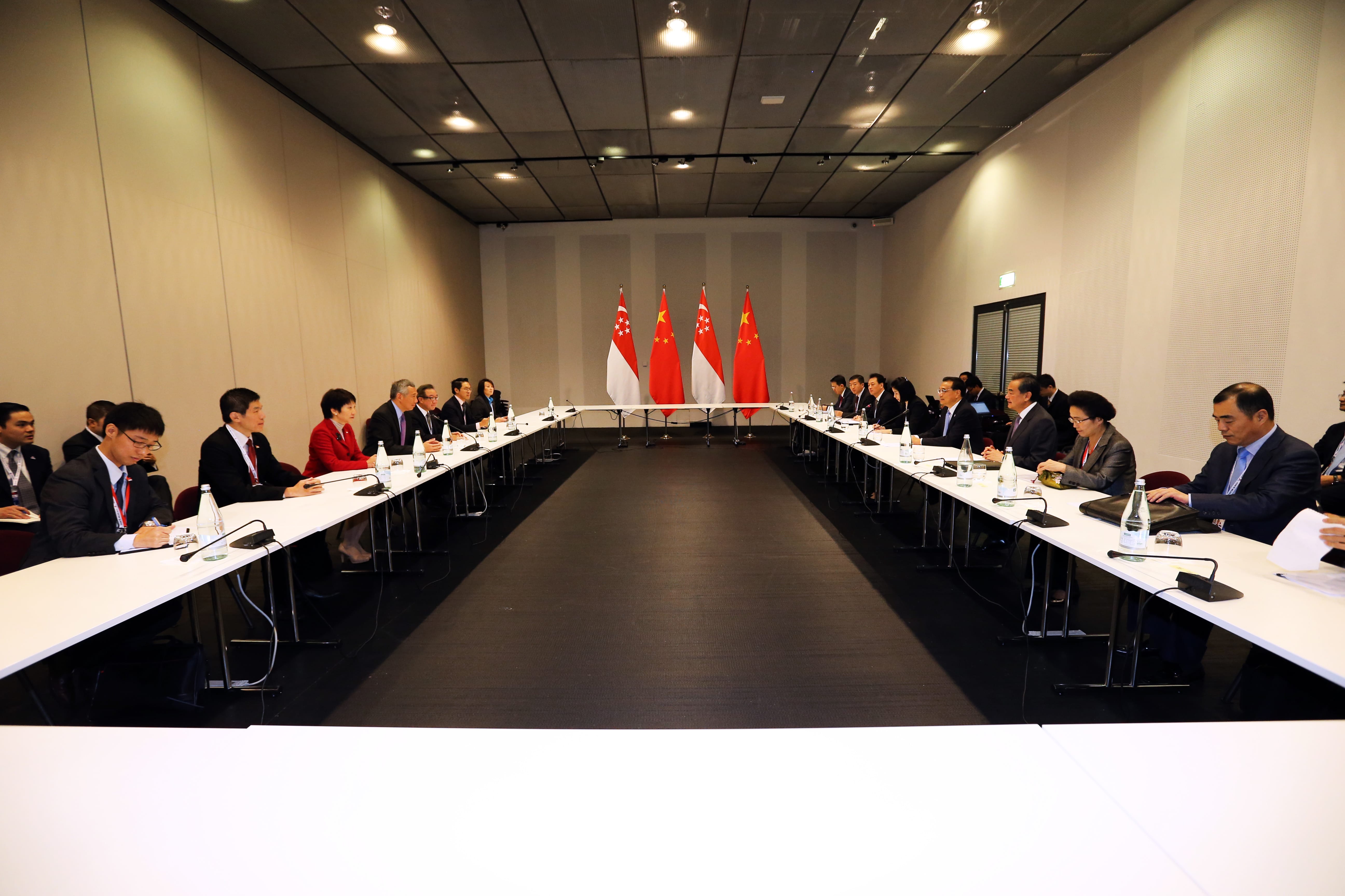 People seated at a long table with Singapore and China flags at the far end.