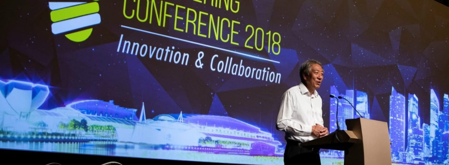 Man at lectern with "Conference 2018" and city skyline on screen behind.