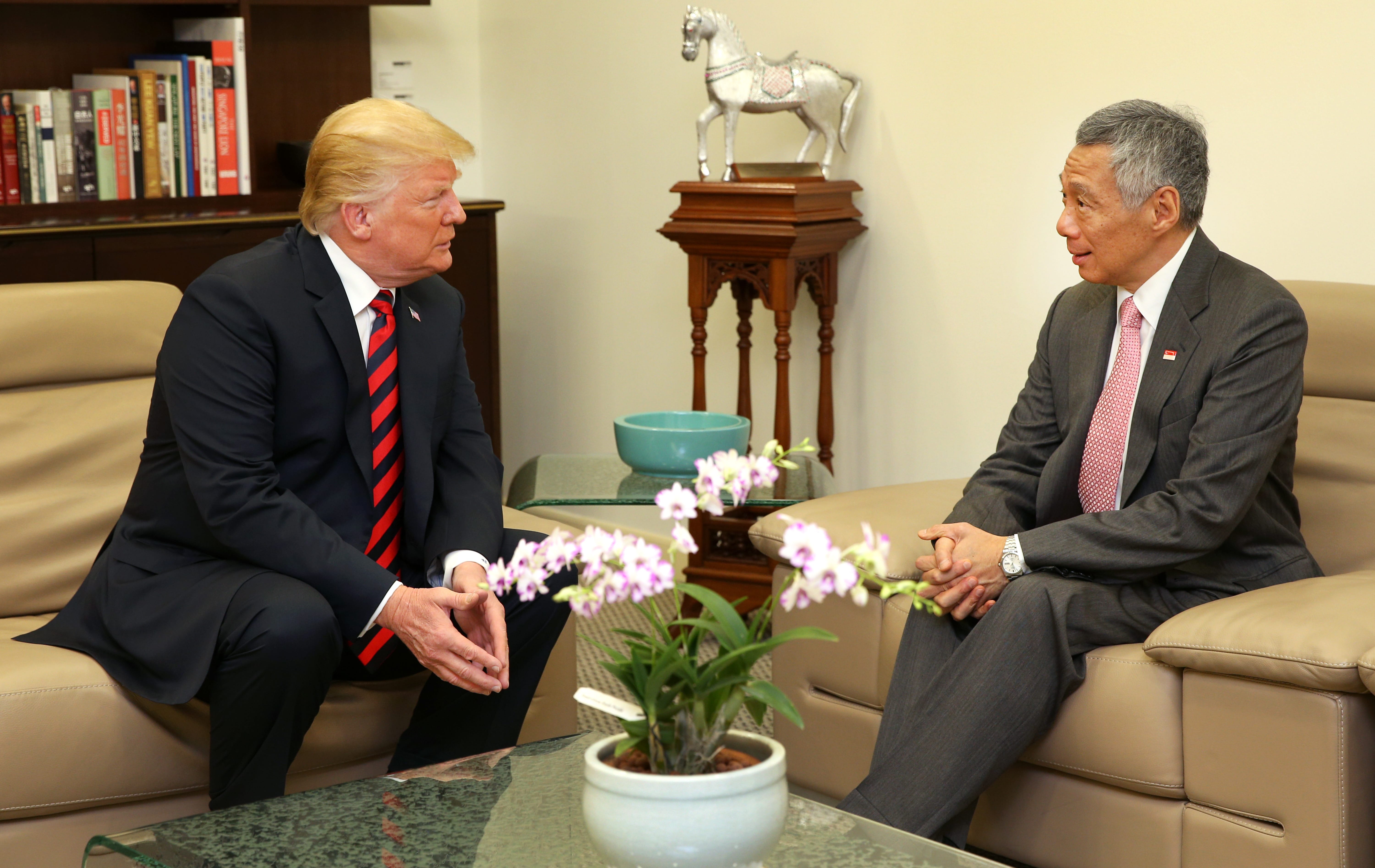 Donald Trump and Lee Hsien Loong sit facing each other on a tan couch.