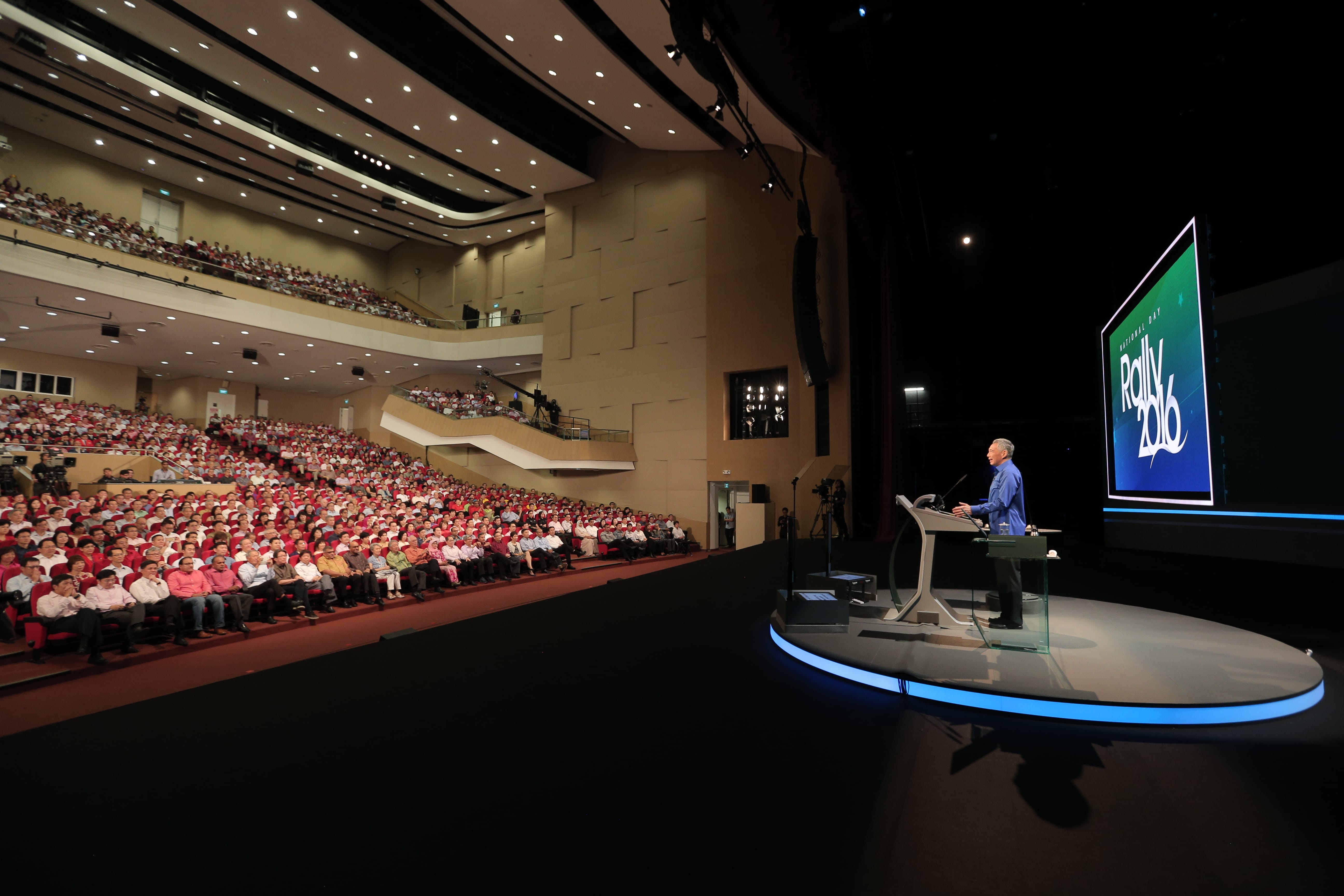 Lee Hsien Loong speaks onstage to a packed auditorium. Screen displays "Rally 2016" logo.