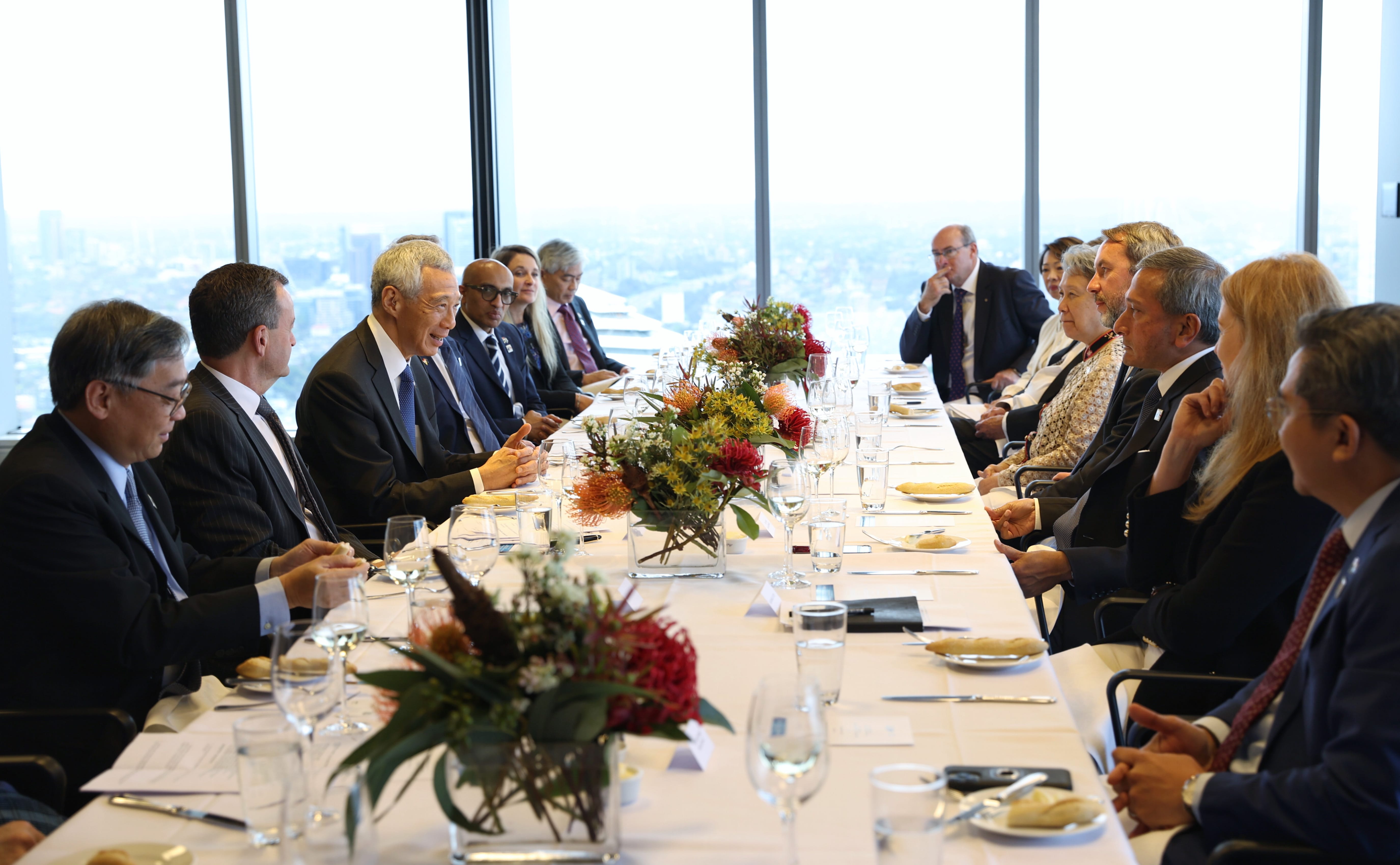 Lee Hsien Loong at a table with diverse people and floral centerpieces in a high-rise building.