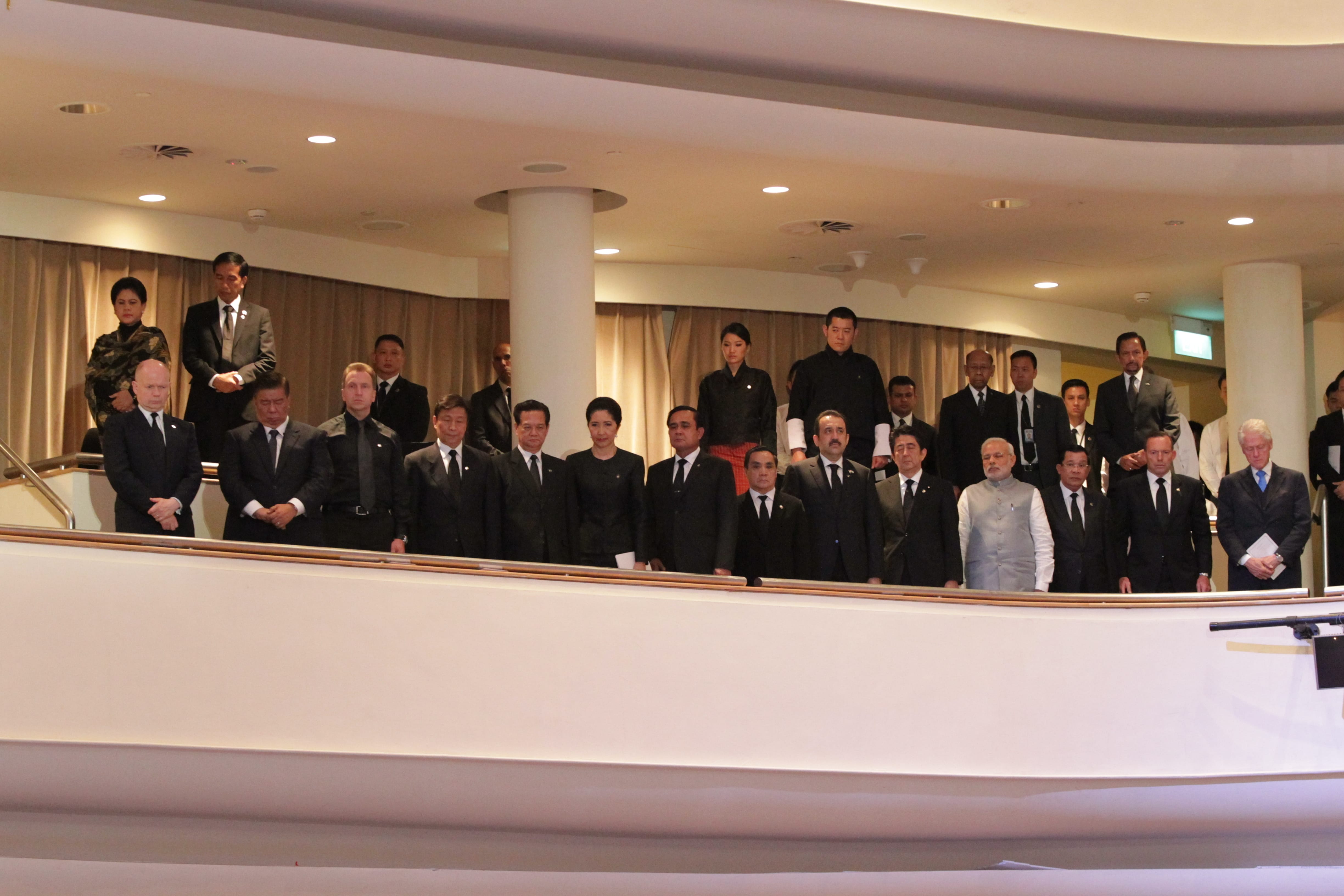 Group of people in business attire standing on a balcony indoors.