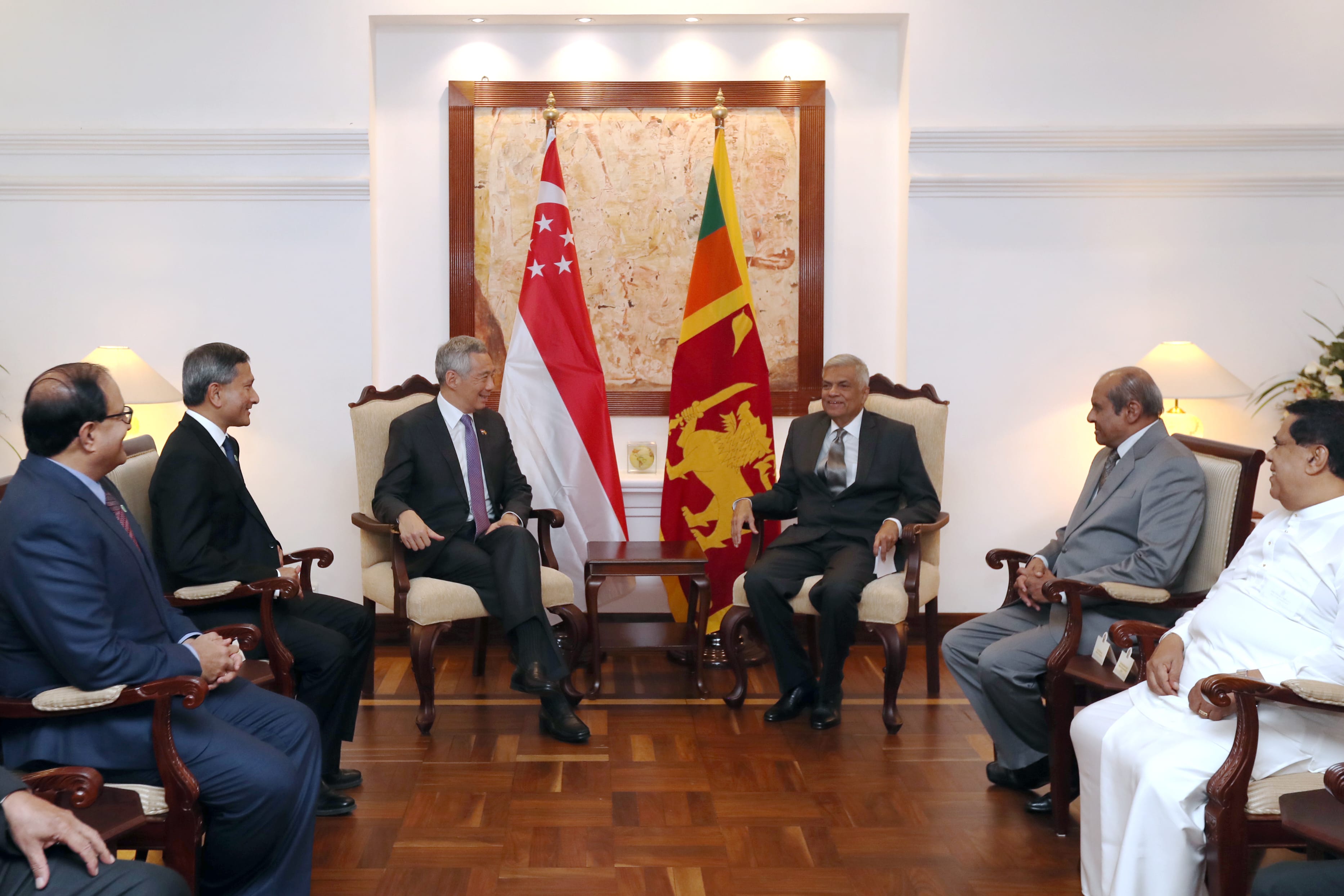 Group of men in suits sit in chairs facing each other; Singapore and Sri Lanka flags in background.