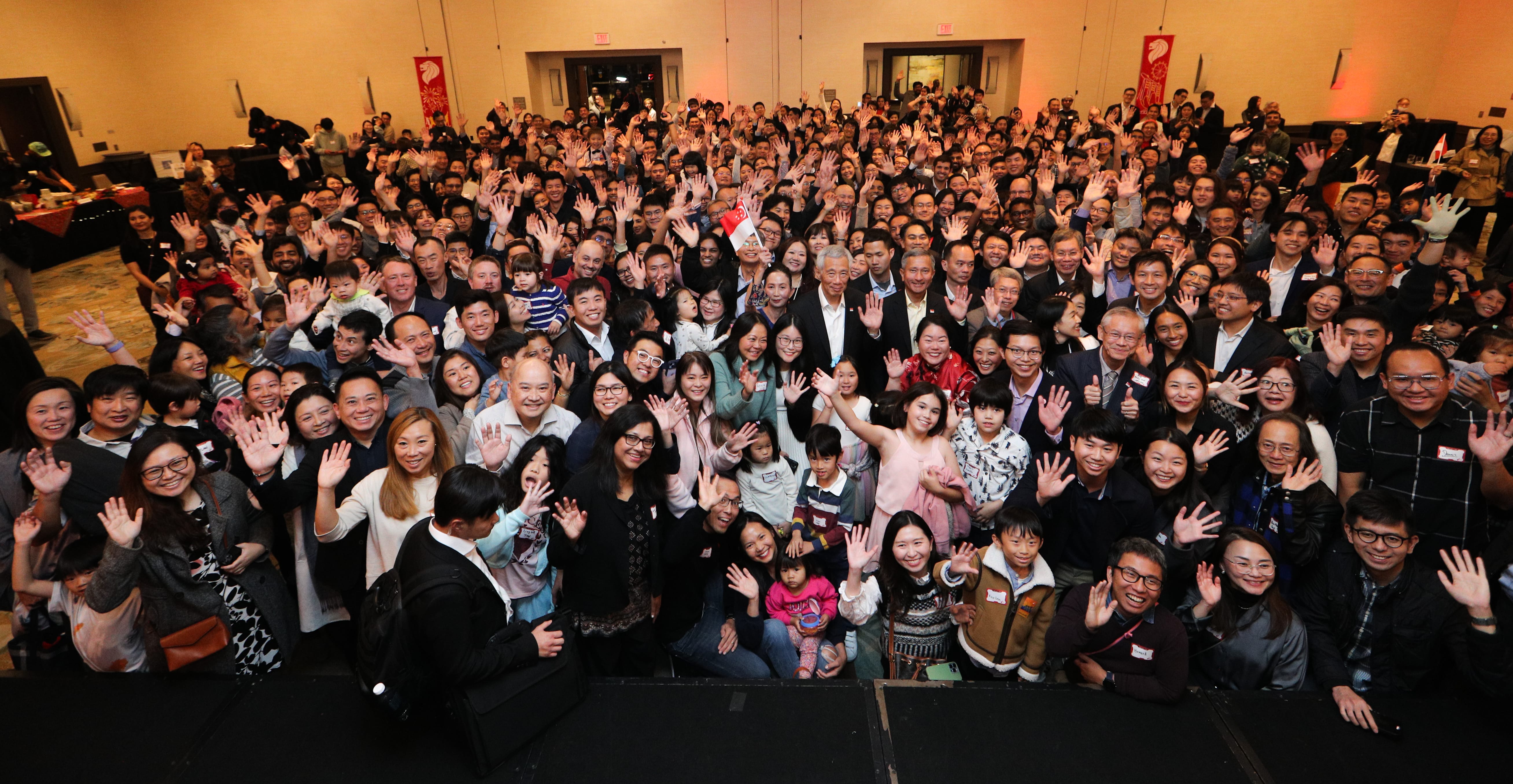 Large group waving indoors; many Asian people, some holding Singapore flags.