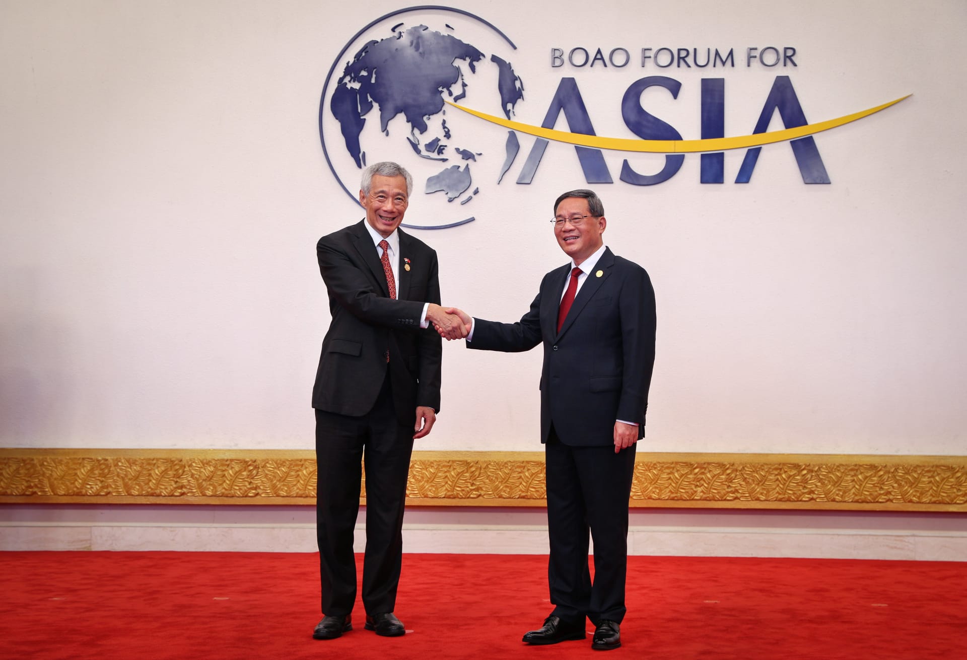 Two men in suits shake hands in front of a Boao Forum for Asia logo.