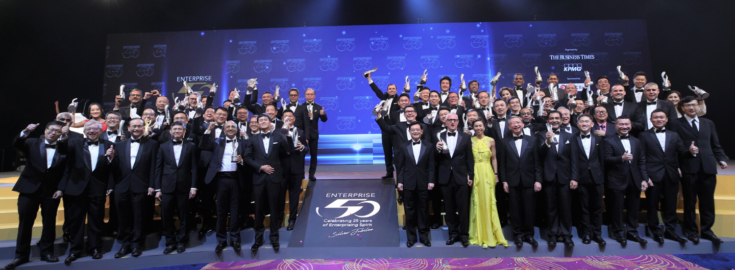 Group of people in formal wear on stage holding awards with "Enterprise 50" backdrop.