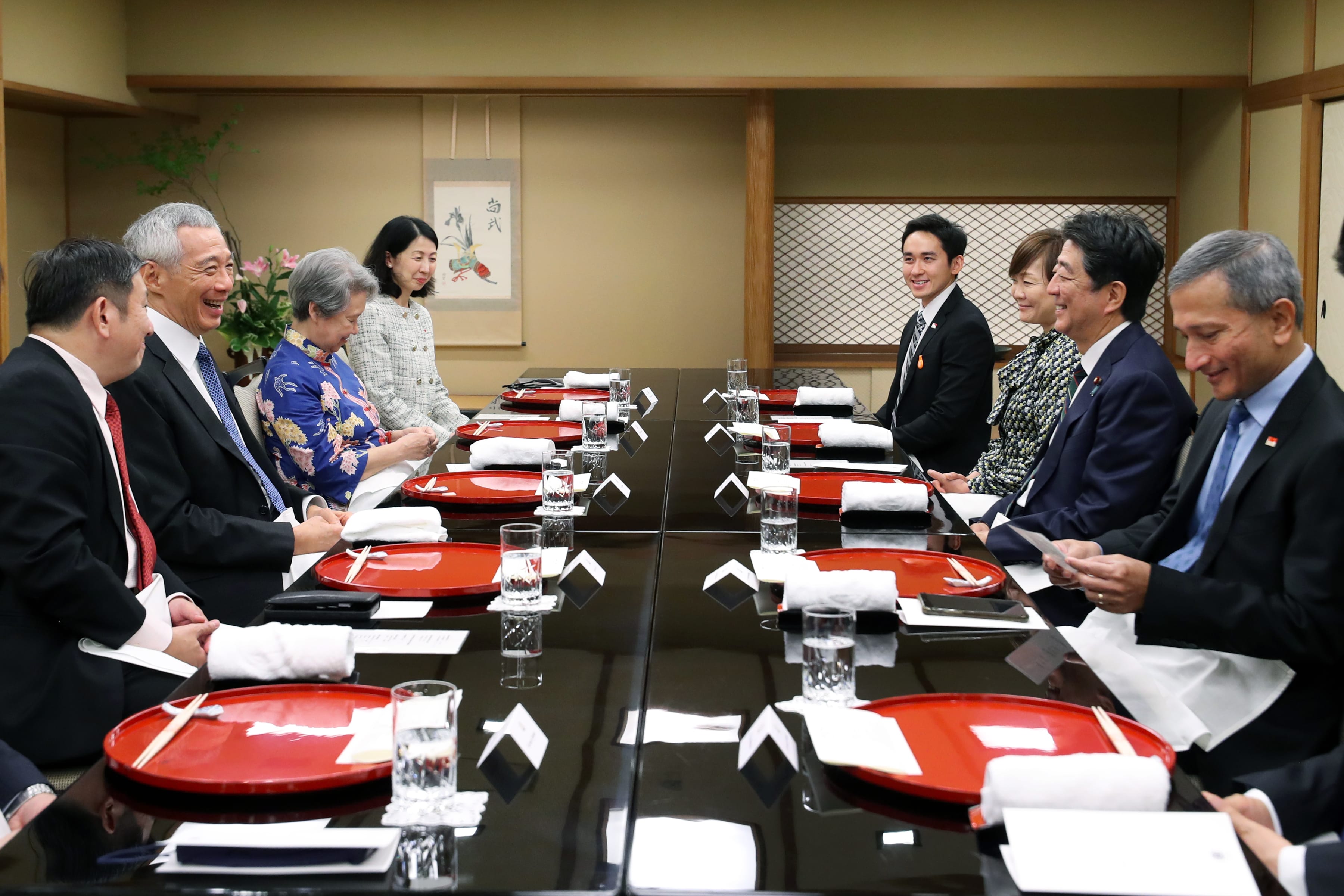 People seated at a long table with red trays, chopsticks, water glasses and white napkins.