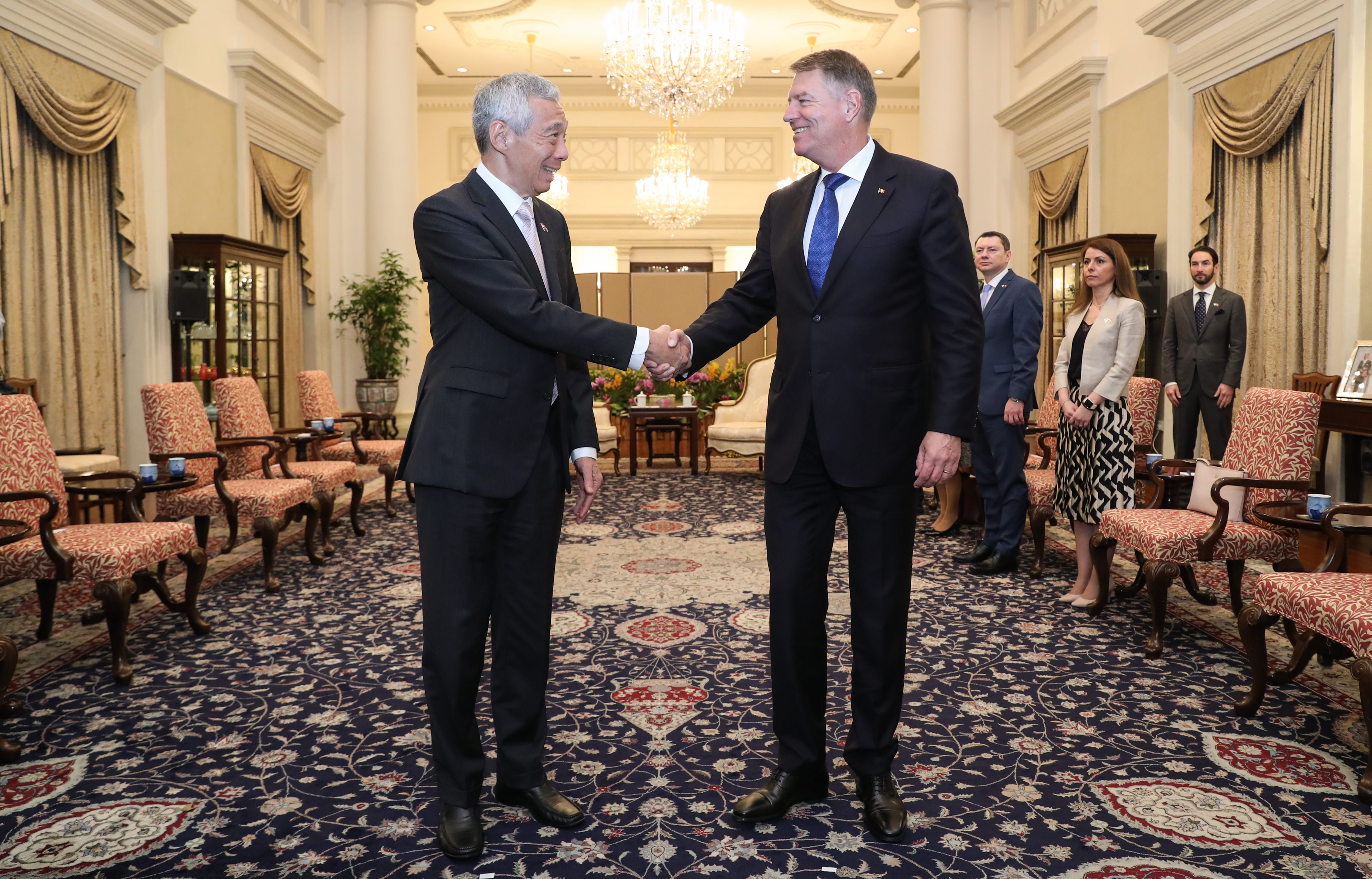 Lee Hsien Loong and Klaus Iohannis shake hands in a formal room with other people.