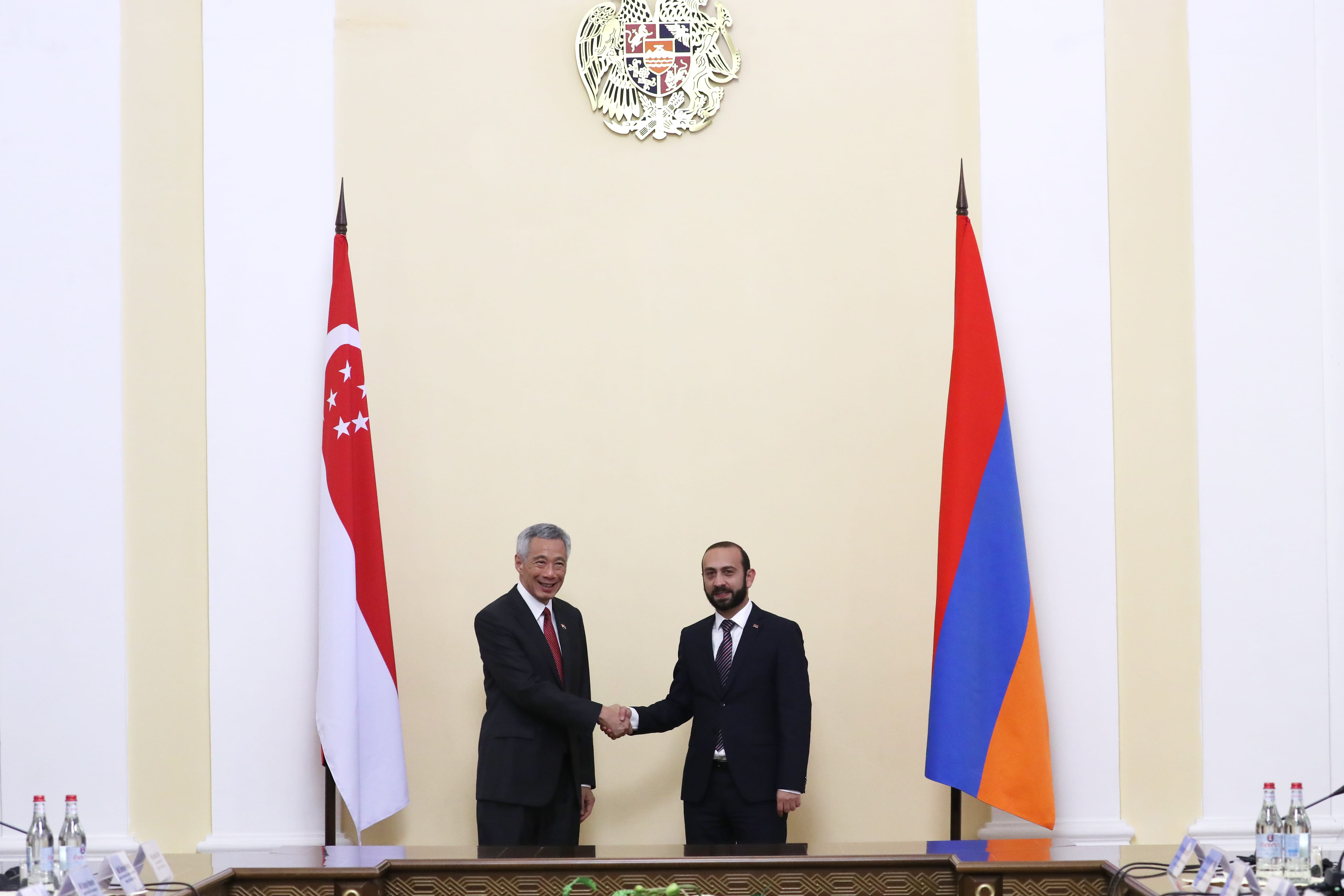 Lee Hsien Loong and Ararat Mirzoyan shake hands between flags of Singapore and Armenia.