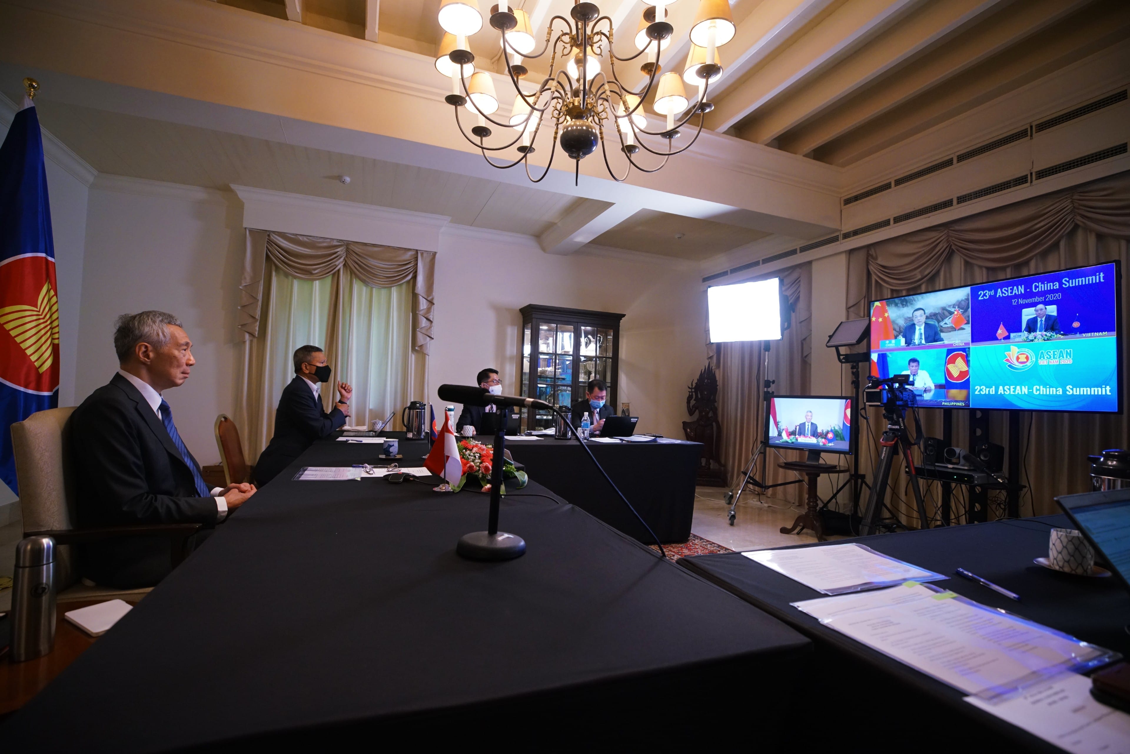 People with masks seated at a table, flags. Monitors display "ASEAN-China Summit."