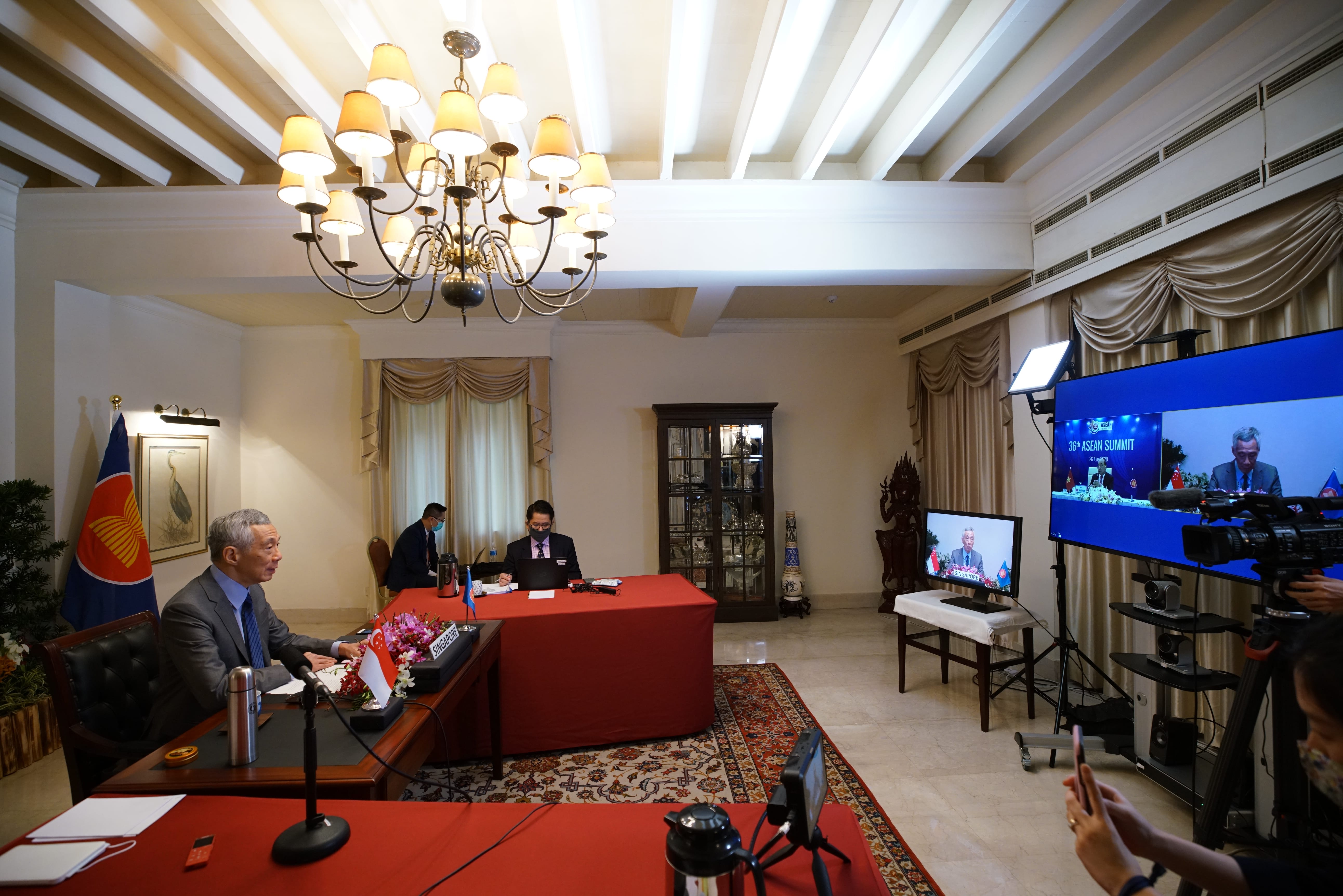 Lee Hsien Loong at desk, virtual summit shown on screens, camera crew records.
