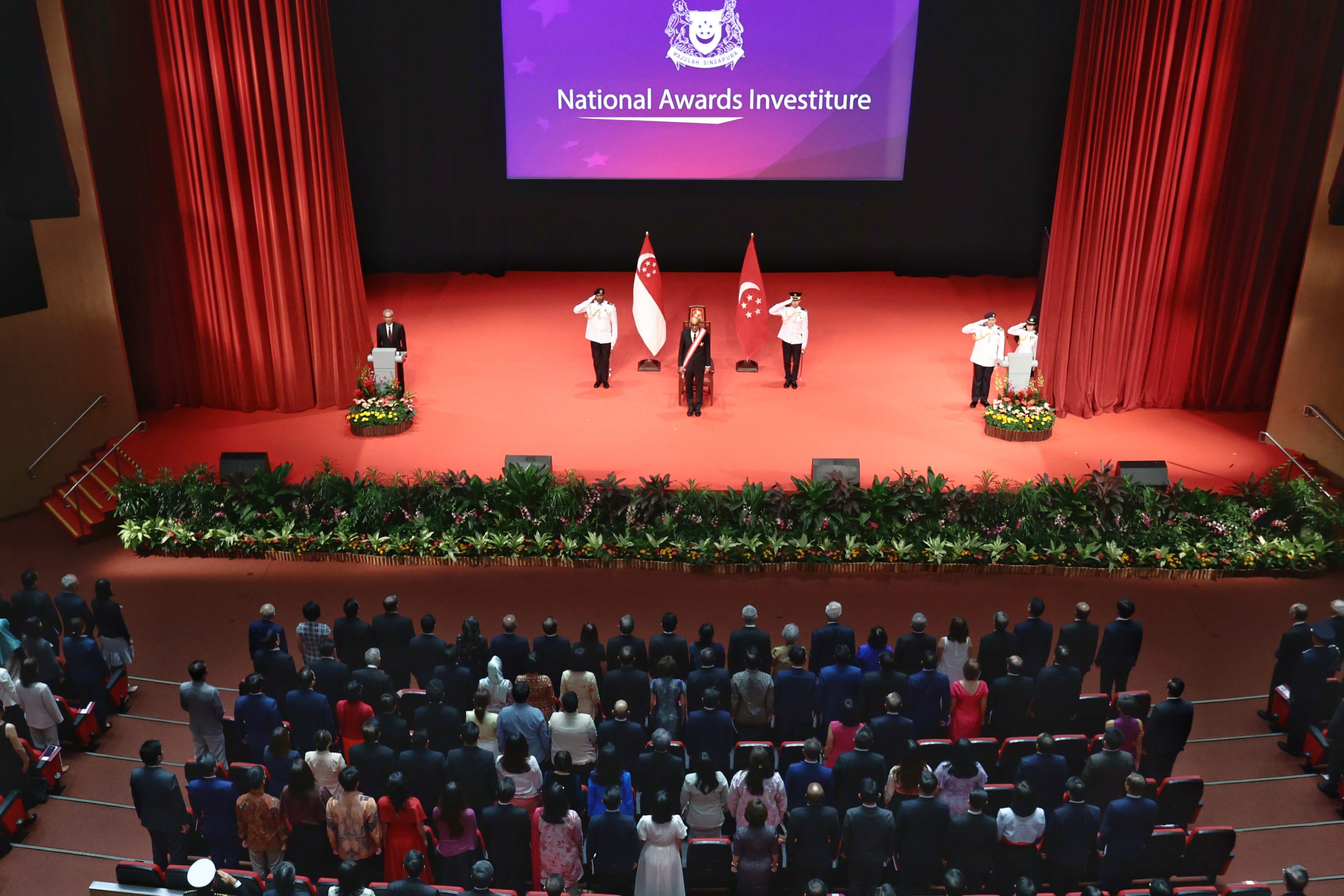 Recipients standing up in an auditorium facing the stage.