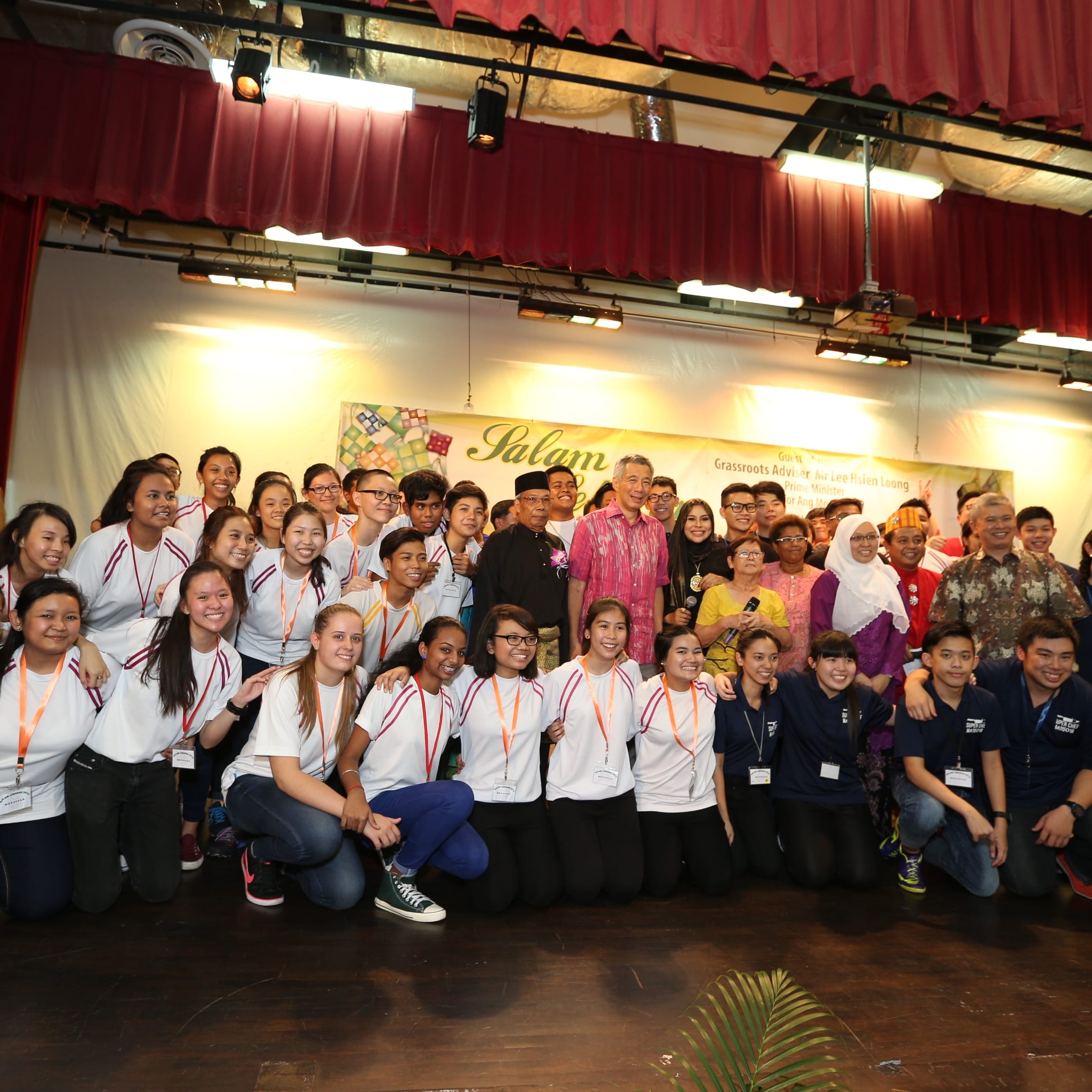 Large group of people on stage, including Lee Hsien Loong, in front of a "Salam" banner.