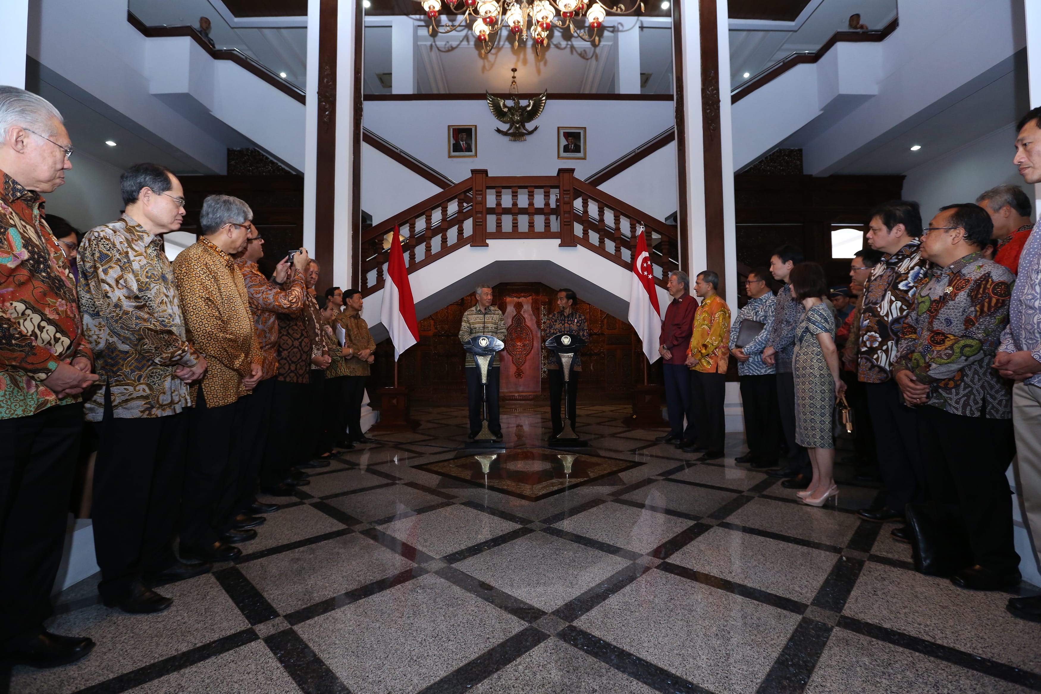 Jokowi & Lee Hsien Loong speak at lecterns flanked by Indonesian and Singaporean flags. Others stand nearby.