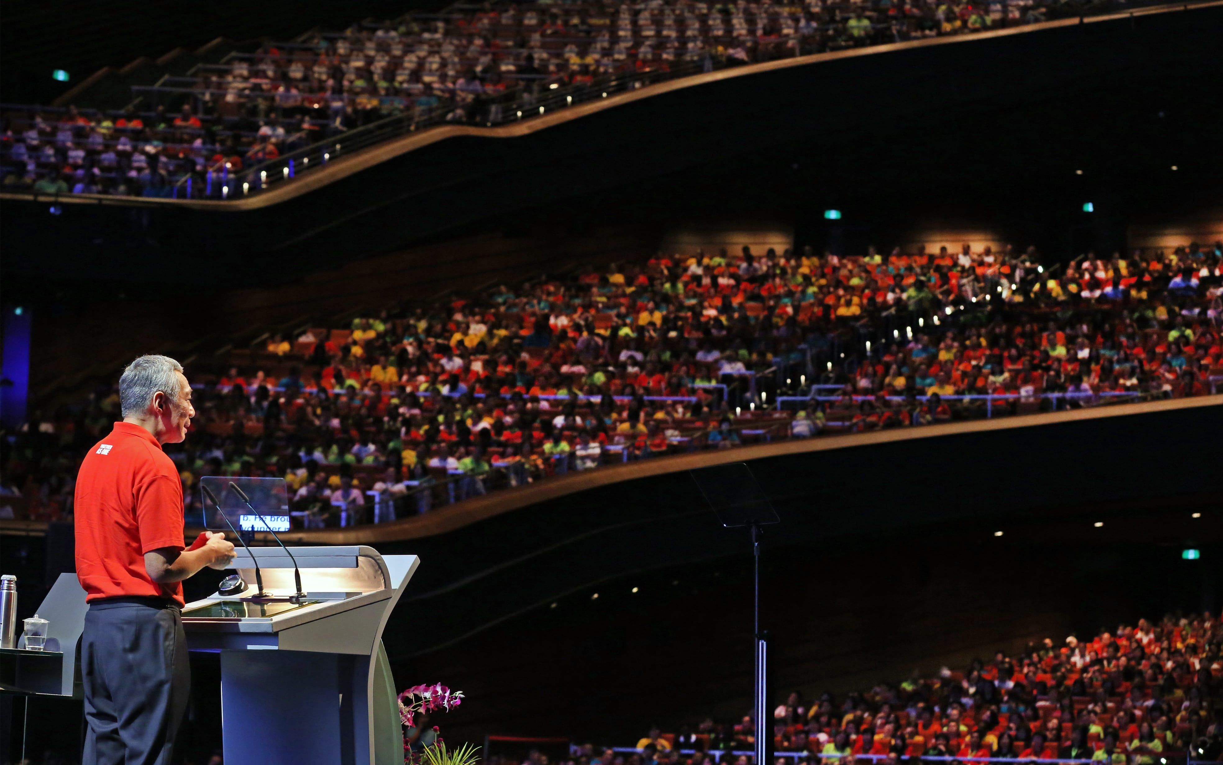 Lee Hsien Loong at podium addressing crowd in a tiered auditorium.