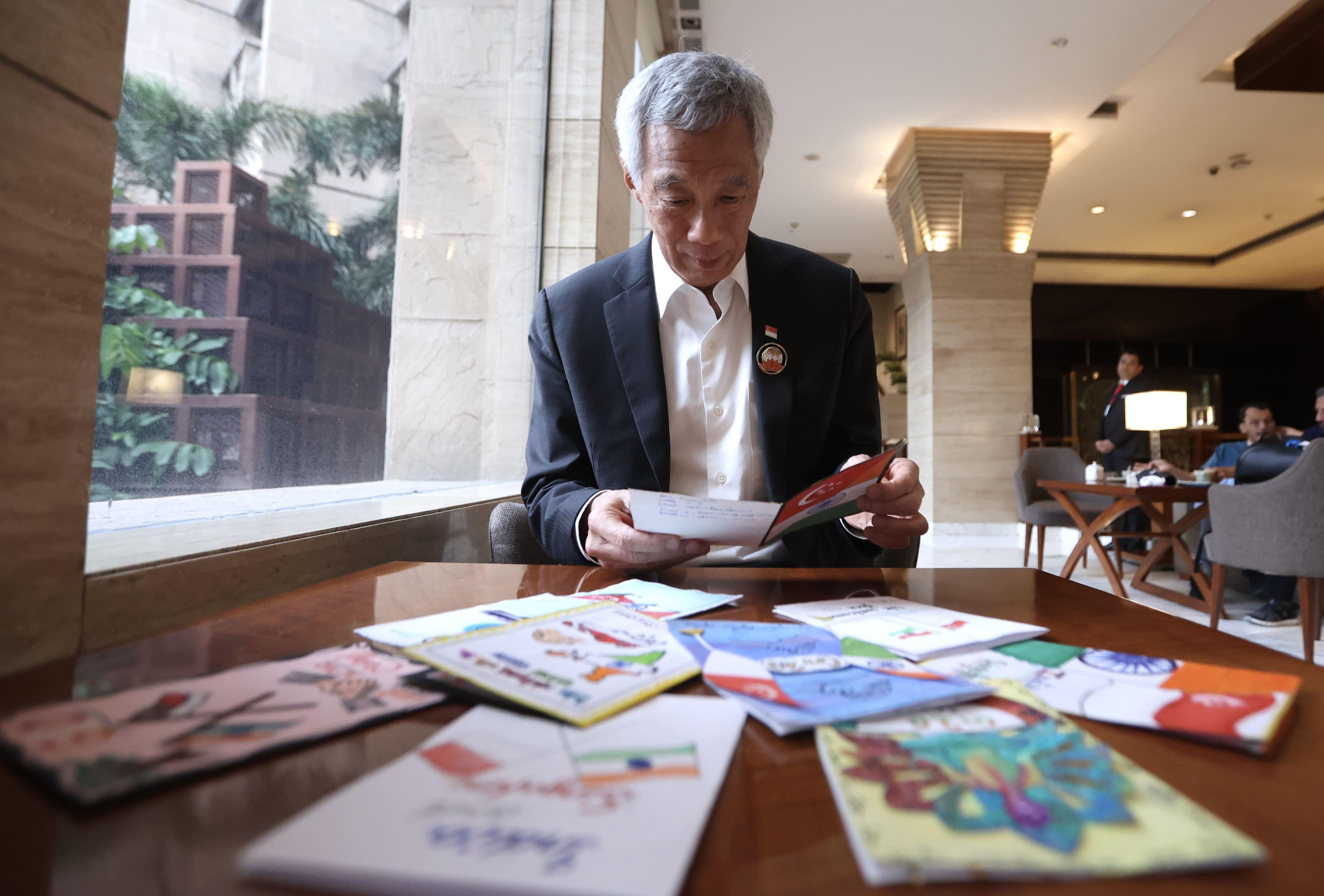 Lee Hsien Loong reading cards at a table. He wears a suit with a Singapore pin.