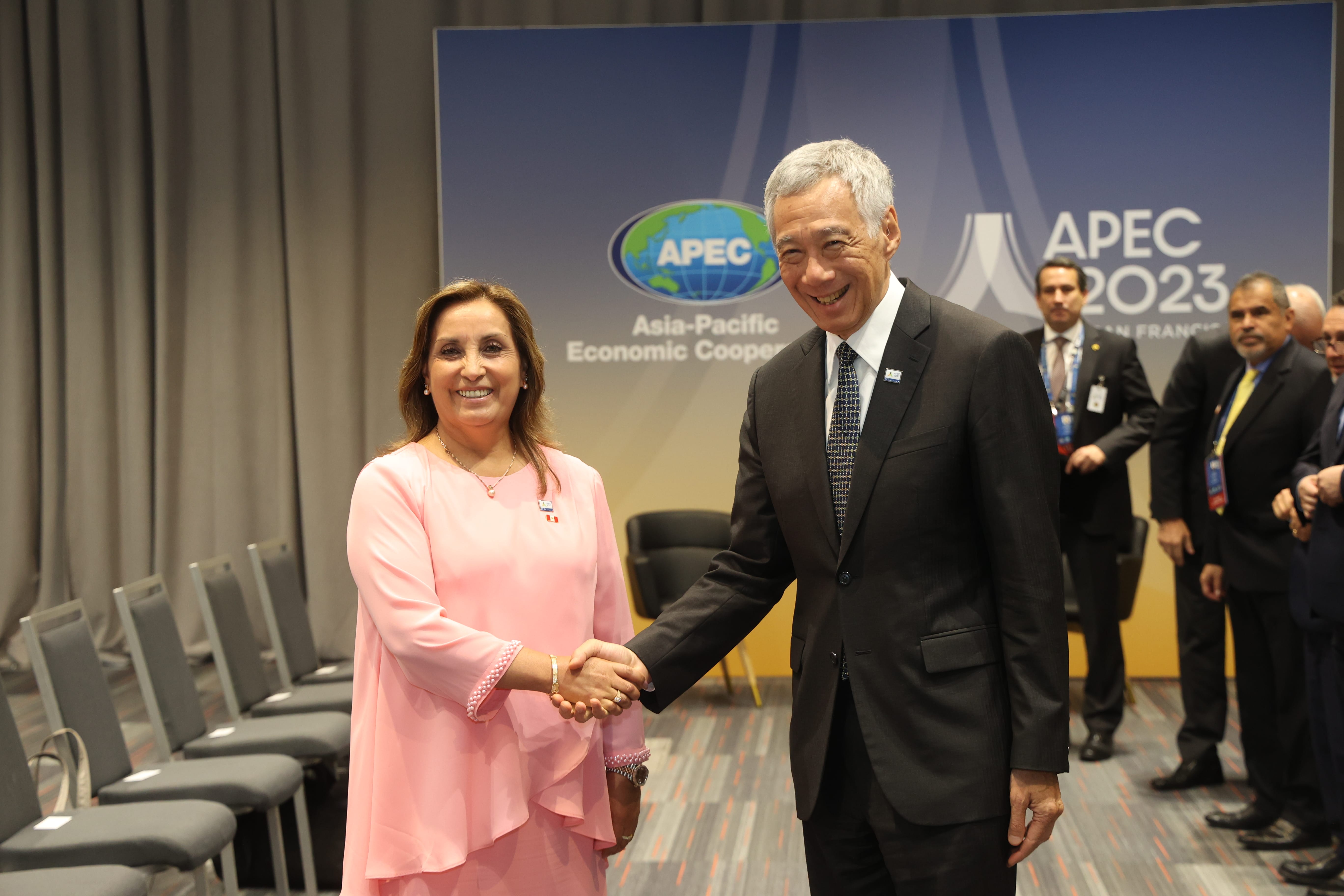 Two people in formal wear shake hands in front of an APEC 2023 banner.