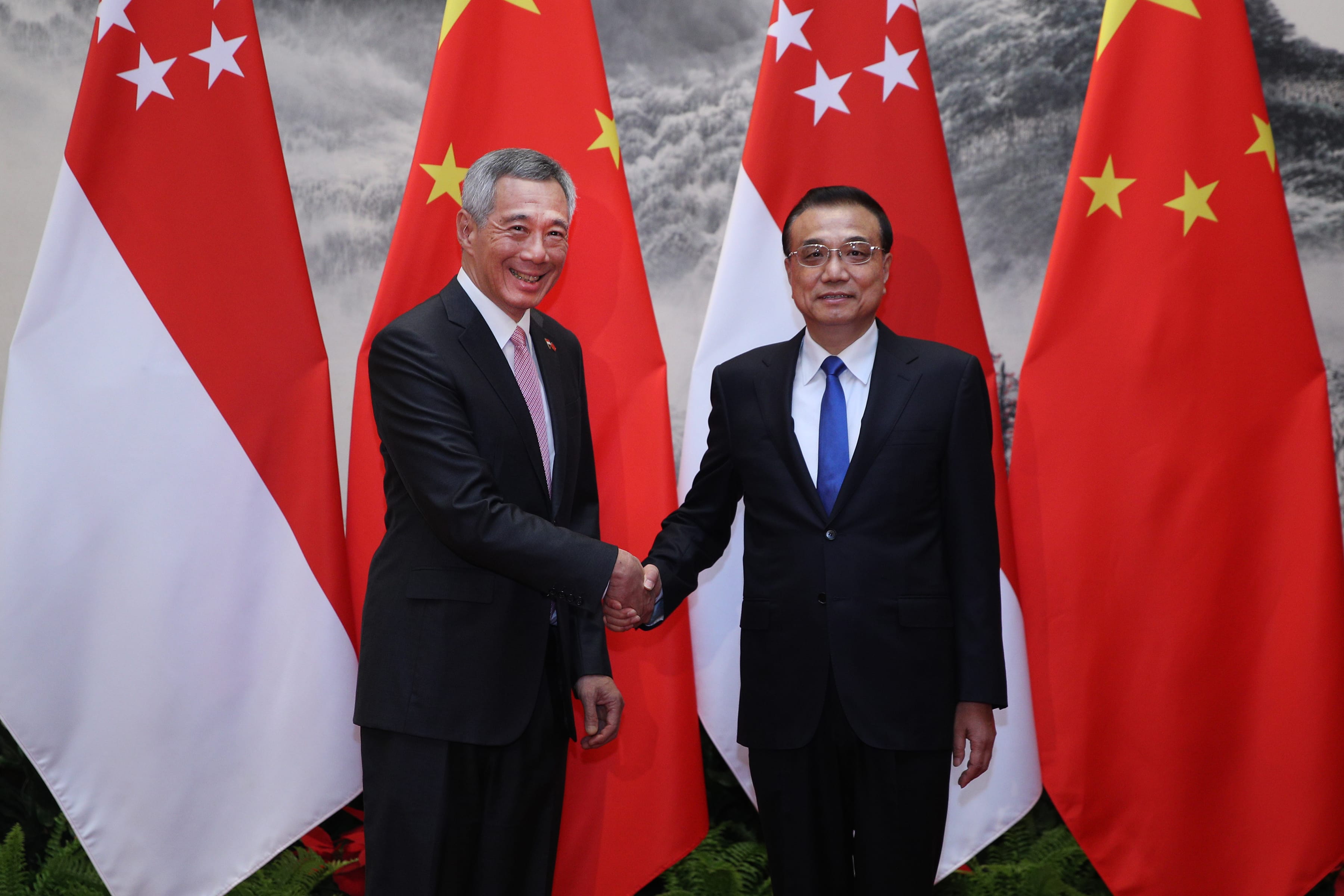 Lee Hsien Loong and Li Qiang shake hands before the Singapore and China flags.