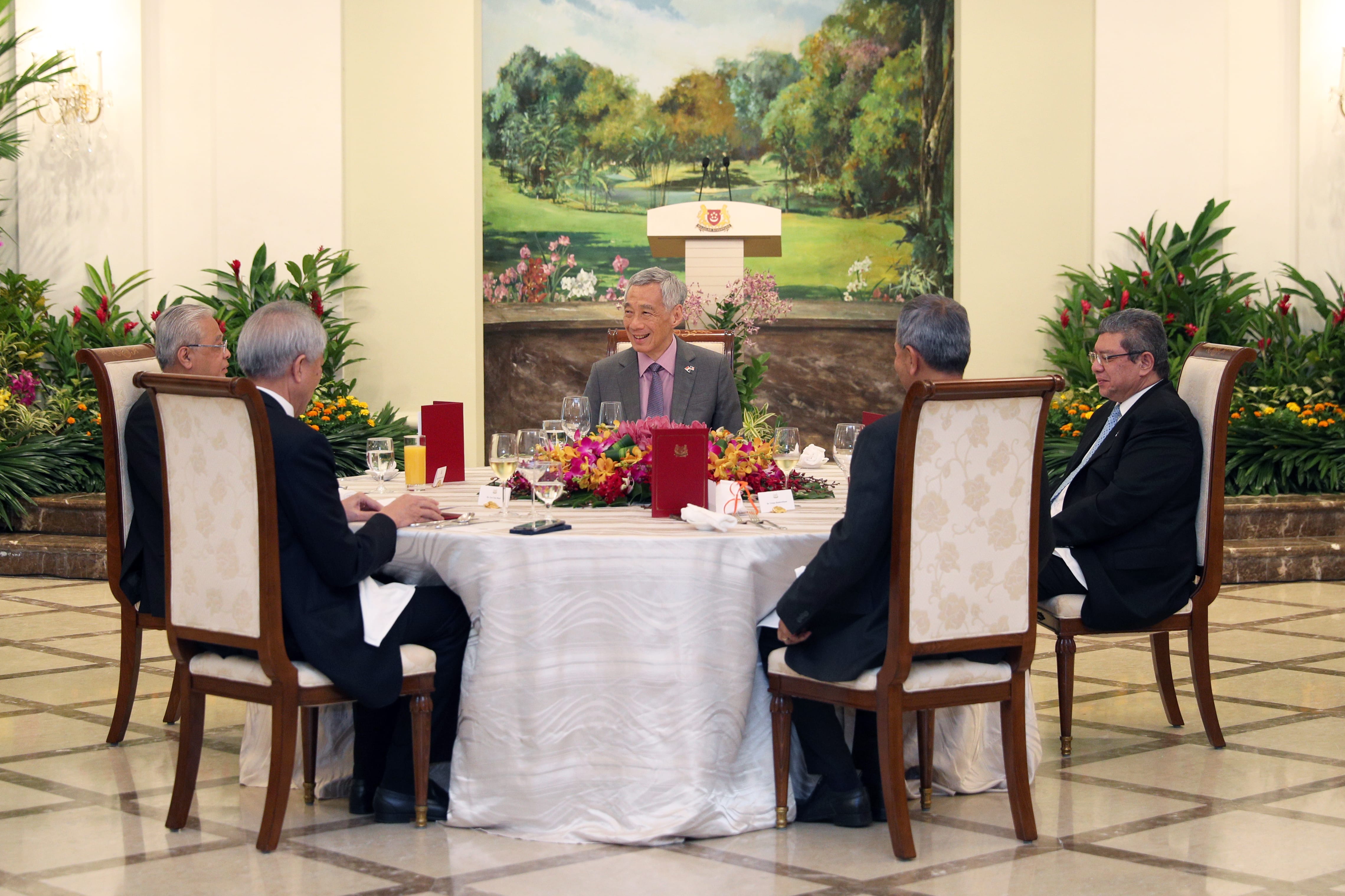 Lee Hsien Loong sits at a round table surrounded by seated men in suits.