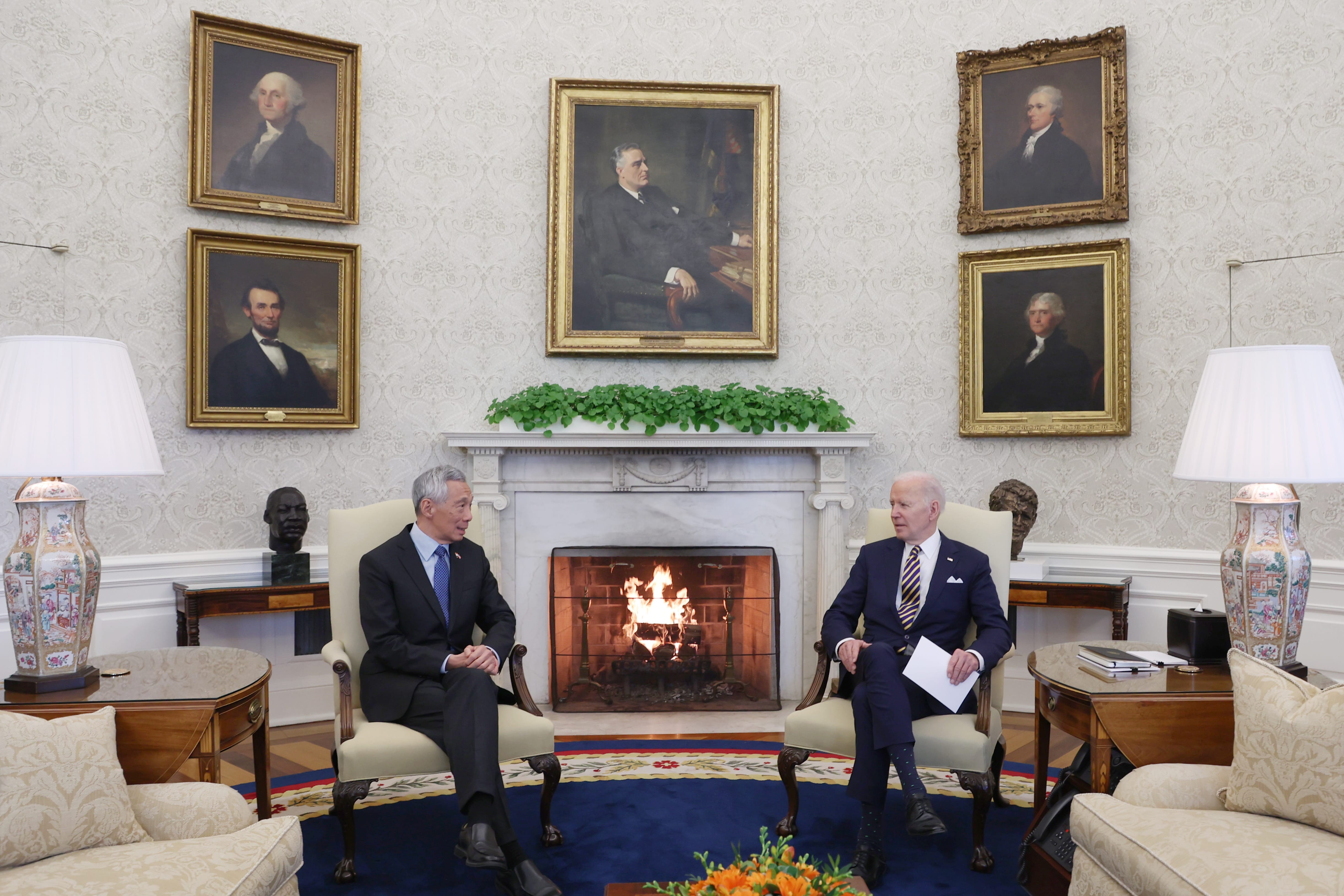 Oval Office setting: Lee Hsien Loong and Joe Biden seated by a fireplace. Presidential portraits on wall.